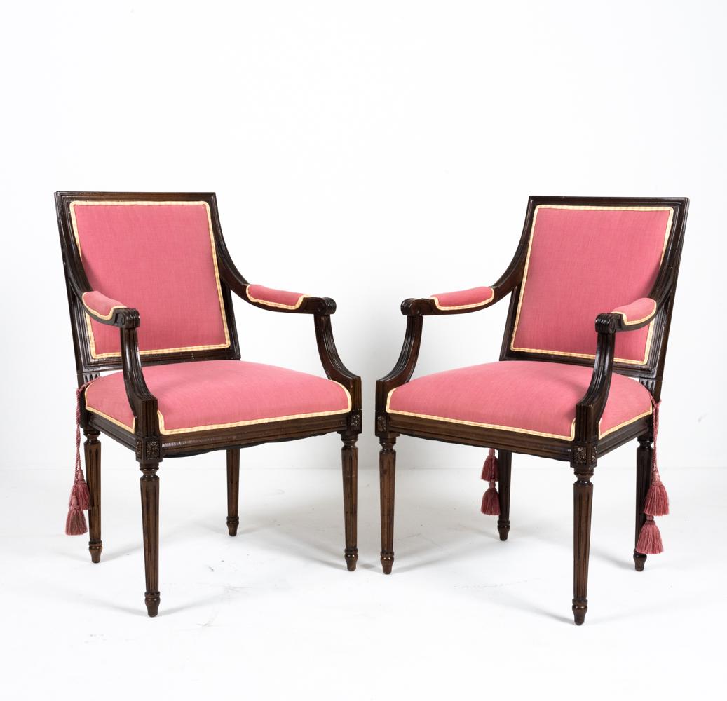 PAIR OF FRENCH LOUIS XVI-STYLE FAUTEUIL ARMCHAIRS: Carved wood frames with fluted legs, rosette details. Removable tassels. Dimensions: H 38.25" x W 24" x D 20.25" x SH 20" Condition: Upholstery with some sun fading and soiling. Wood with some old wor