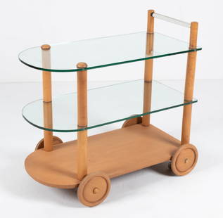 GILBERT ROHDE ART DECO BAR CART, C. 1940'S: Iconic three-tier bar or tea cart in blonde wood and glass, featuring a glass handle and decorative sculpted wood wheels. Dimensions: H 32" x W 34" x D 19.75" Condition: Great candidate for restoratio