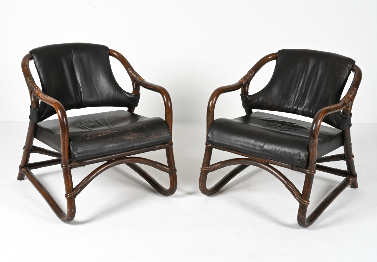PAIR OF VINTAGE RATTAN & LEATHER ARMCHAIRS: (2) Mid-Century pole rattan and brown leather armchairs with beautifully contoured lines in the manner of Cerda Stuhl. Circa 1960s. Dimensions: H 30.25" x W 24" x D 30" x SH 17" Condition: Minor surfa