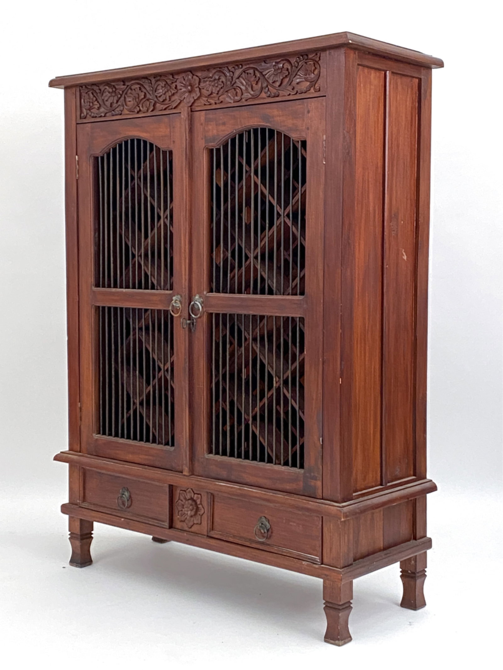 VINTAGE WINE CABINET: Possibly of Asian manufacture. European-style floral carving. Interior with fitted racks. Brass rods through the doors. Dimensions: H 54.75" x W 40.25" x D 16" Condition: Some surface distress. break 
