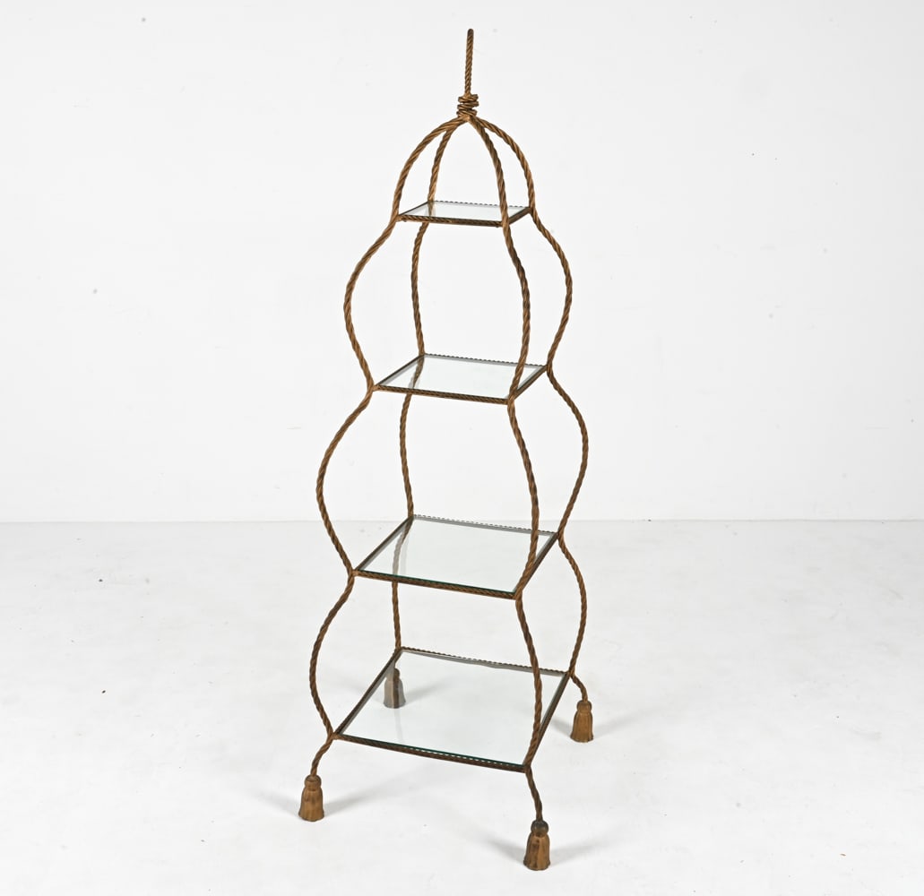 HOLLYWOOD REGENCY STYLE ROPE & TASSEL ETAGERE: Gold-finished metal and glass. Dimensions: H 61" x W 20.5" x D 20.5" Condition: Possible repair to one foot. Metal with patina and finish losses throughout. Scratches and a few scallops to glass.