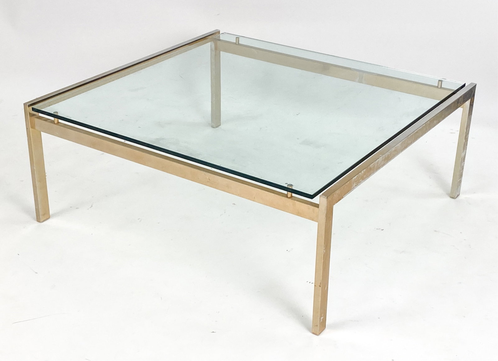 MODERN GLASS TOP COFFEE TABLE: Chrome base with gold-tone finish, glass top. Dimensions: H 15" x W 38.5" x D 36" Condition: Finish losses and wear to base. Scratches to glass. Chip to glass corner.
