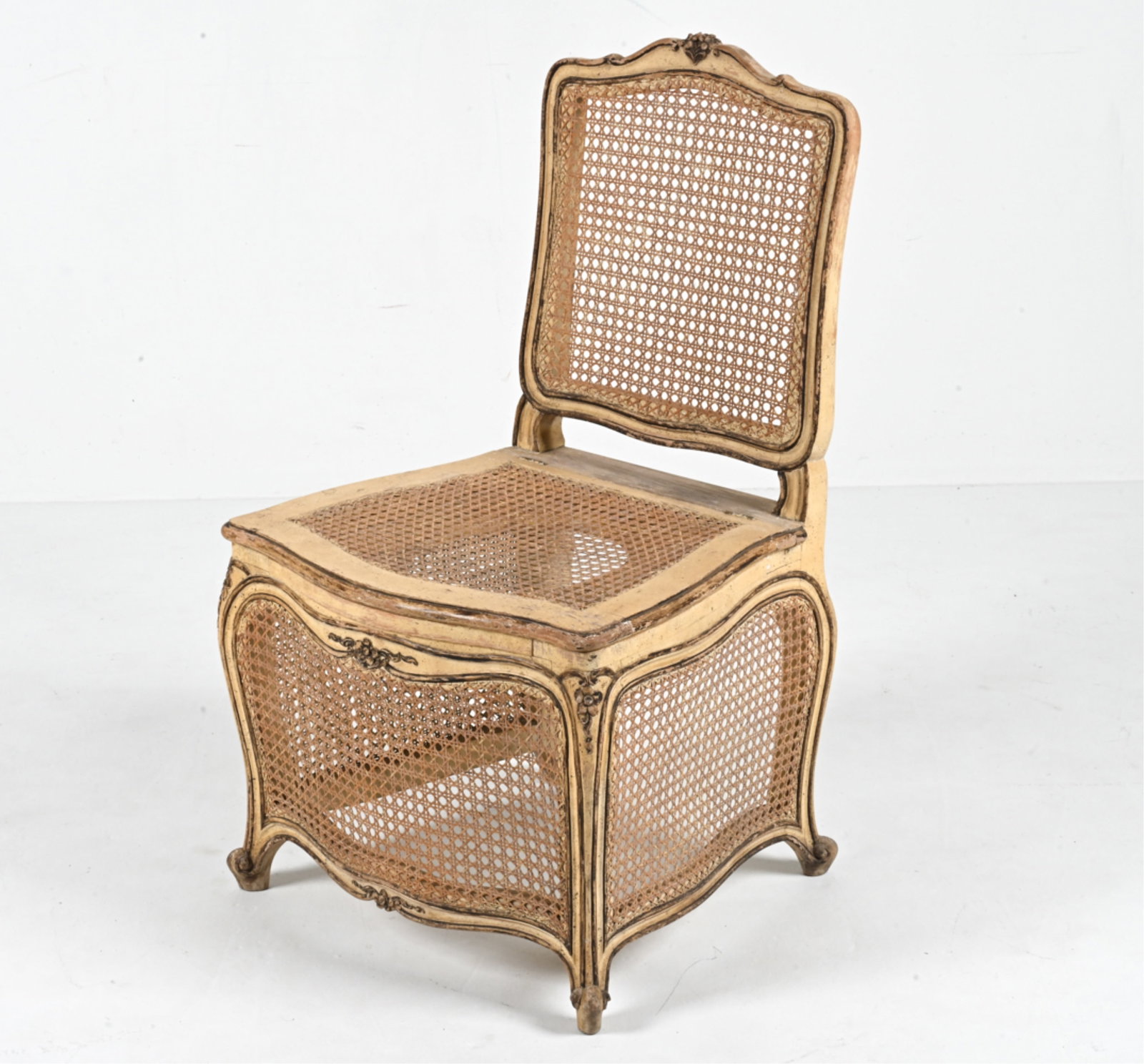FRENCH PROVINCIAL CANED COMMODE CHAIR: C. Early 20th Century; labeled Invincible Parlor Frame Co. underneath. Dimensions: H 38" x W 22.5" x D 21.5" x SH 17.75" Condition: Distressed paint throughout; minor joint separation to frame. Proven