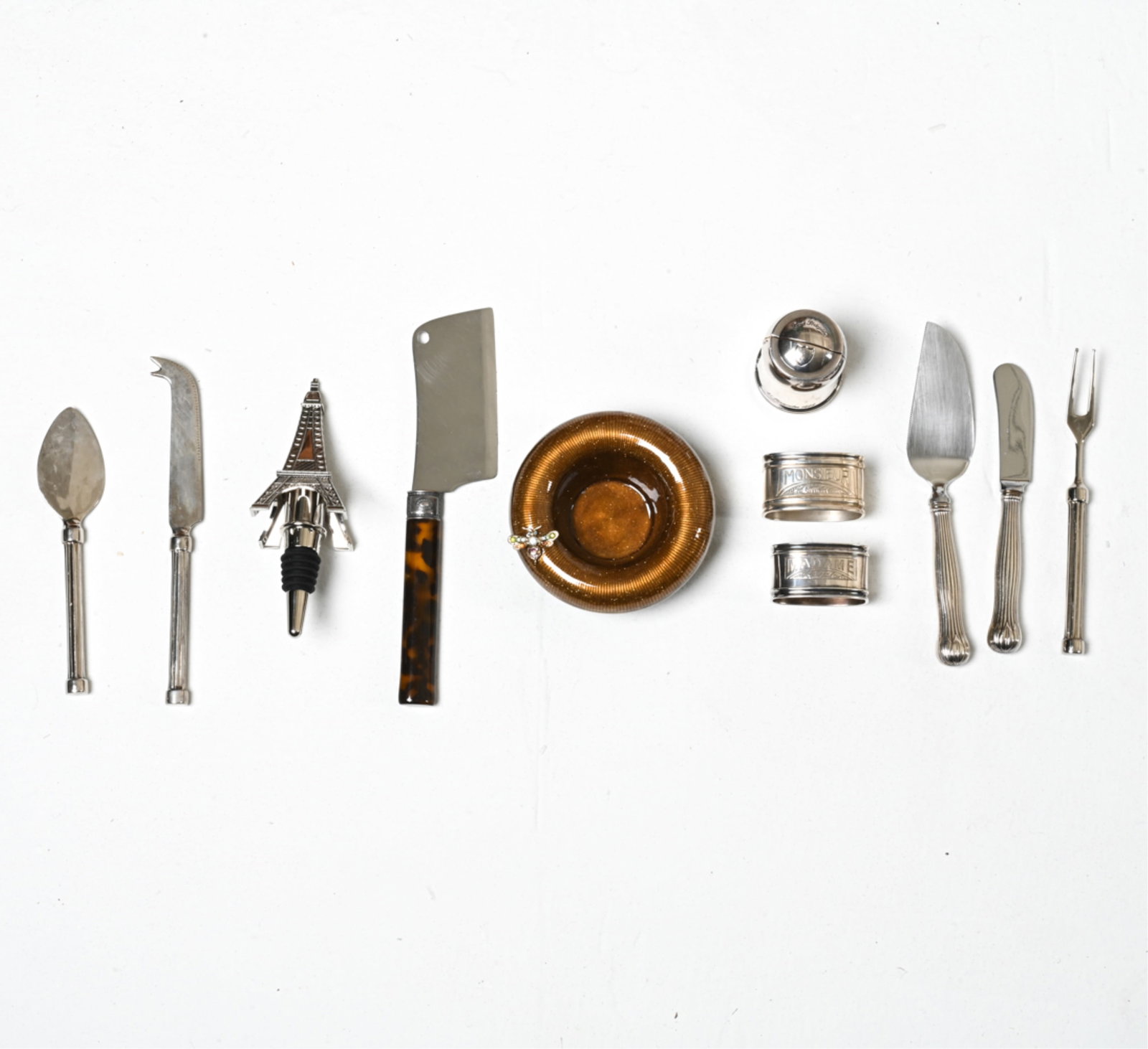 GROUPING OF DECORATIVE TABLEWARE & OBJETS DE VERTU: Including a silverplate cork keeper by Christofle for Dom Perignon, Tiffany & Co. cheese knife set with sterling handles, enamel vide poche by Jay Strongwater, and various others. Dimensions: (Jay Str