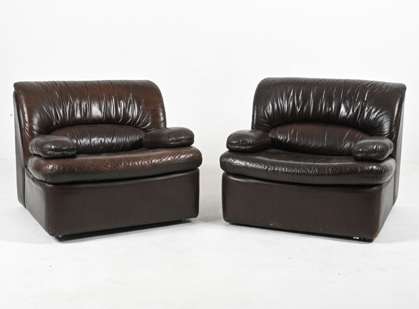 PAIR OF DE SEDE STYLE LEATHER LOUNGE CHAIRS: Late 20th Century. Dimensions: H 29.5" x W 34" x D 39.75" x SH 16" Condition: Missing one caster. Leather in very good vintage condition; a few small marks and rubs. Damages to castors, one missing a
