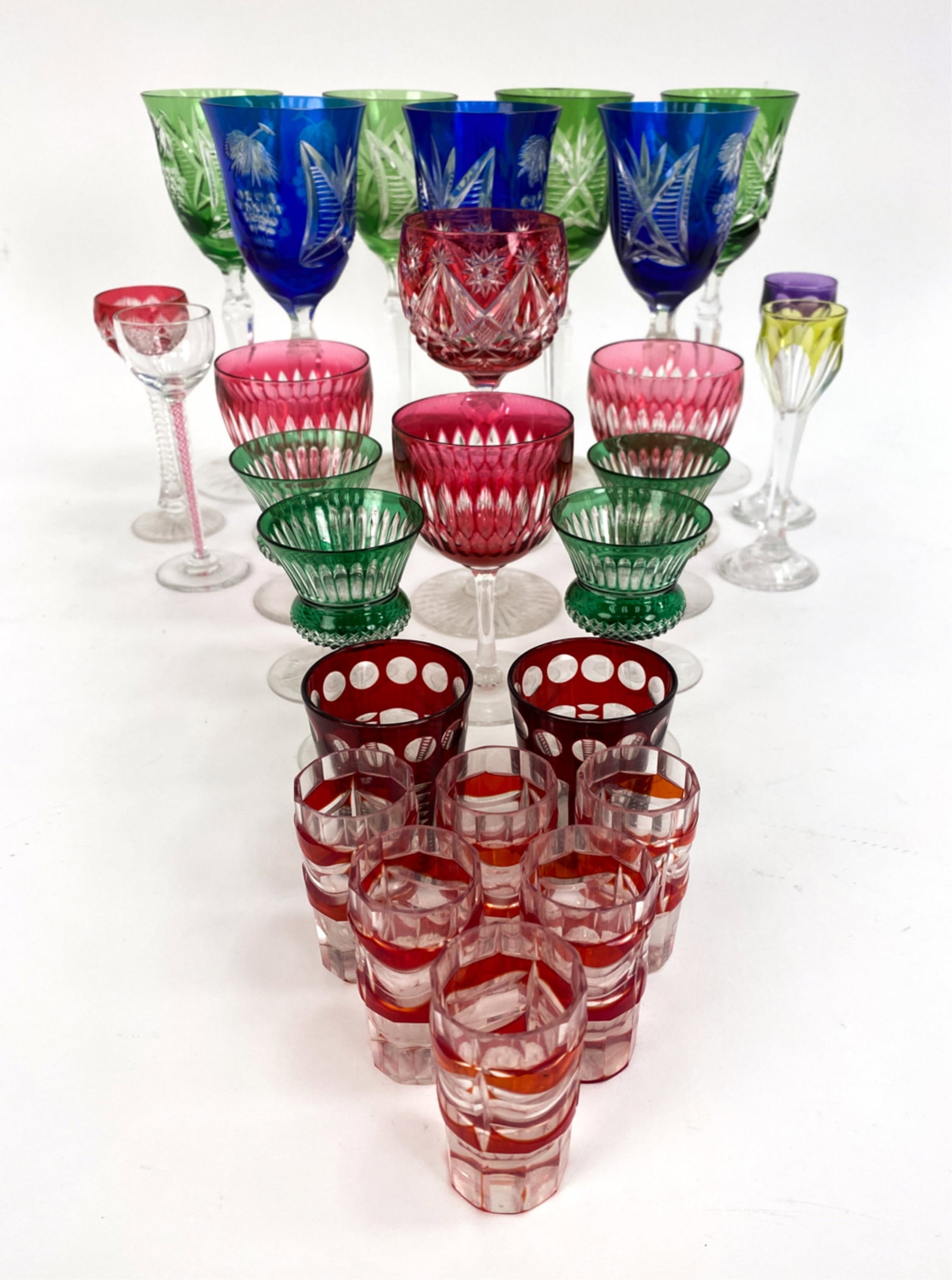 GROUPING OF CUT TO CLEAR COLOR GLASSWARE: Variety of cut-to-clear glasses includes, cordials, wine, and shot glasses. Variety of colors and patterns. Dimensions: (Tallest) H 8.25" Condition: Handling wear, no apparent damages.