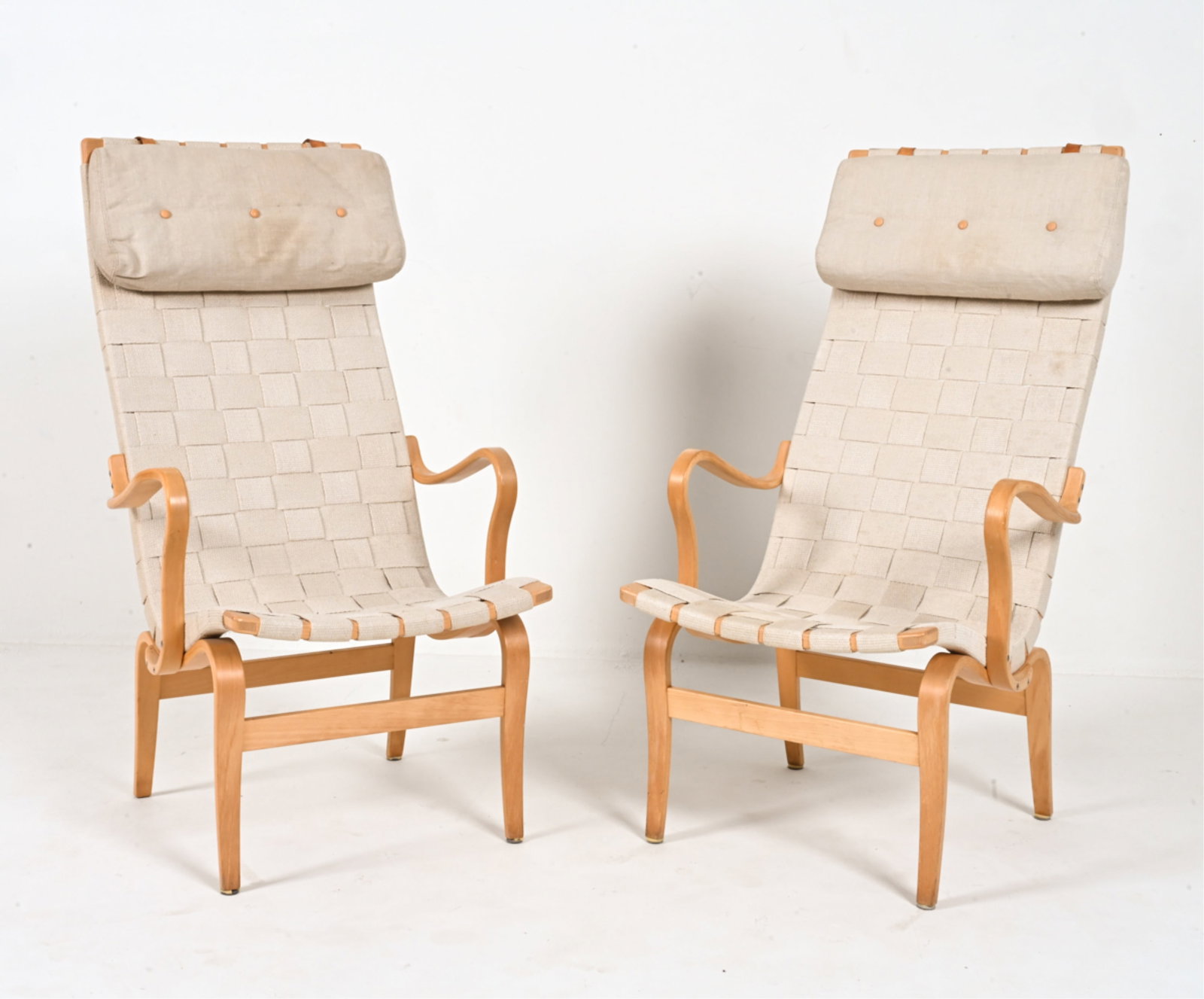 PAIR OF BRUNO MATHSSON FOR DUX PERNILLA CHAIRS: Bent laminated beech wood and woven web strapping, with canvas and leather head cushions. Sweden, c. Late 20th Century. With stamped signature on back stretchers. Dimensions: H 43" x W 24.5" x D 29" x