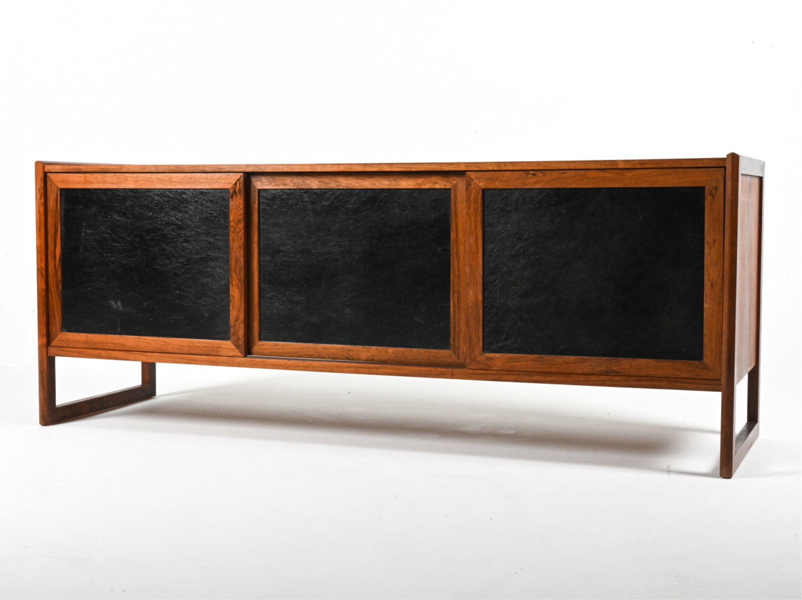 ROSEWOOD & LEATHER PANEL SIDEBOARD, C. 1970'S: In the style of Jens Risom or Jack Cartwright, c. 1970's. Dimensions: H 28"x W 71"x D 21.5" Conditions: Sun fading, a few water spots and minor scratches to wood; a few scuffs and small marks to leath