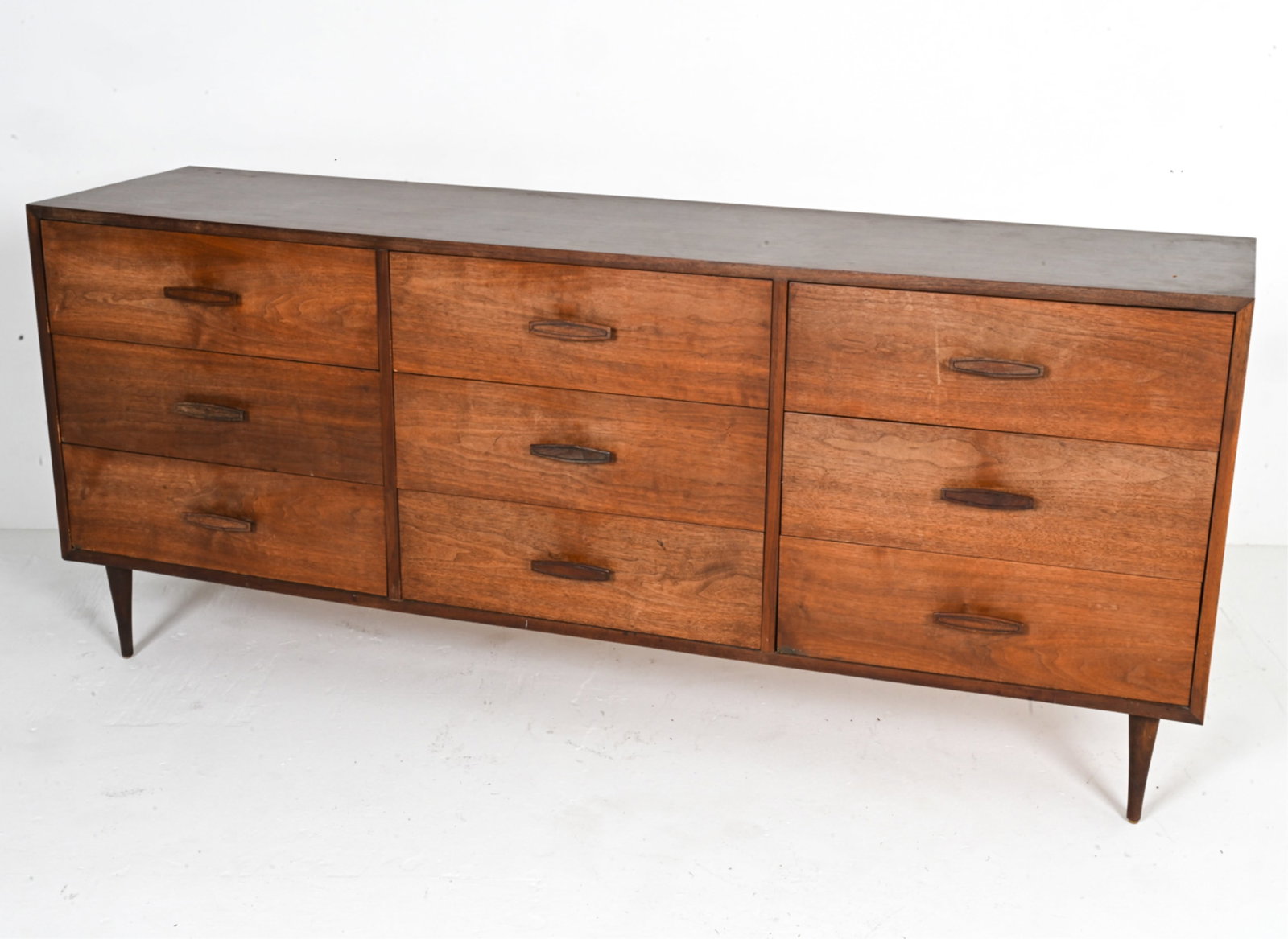 MID-CENTURY CHEST OF DRAWERS: Lowboy dresser with nine drawers. Apparently unsigned, c. 1960's. Dimensions: H 30.5" x W 71.5" x D 18". Condition: Sun fading and water spots to front; a few chips and losses to veneer at edges. A fe