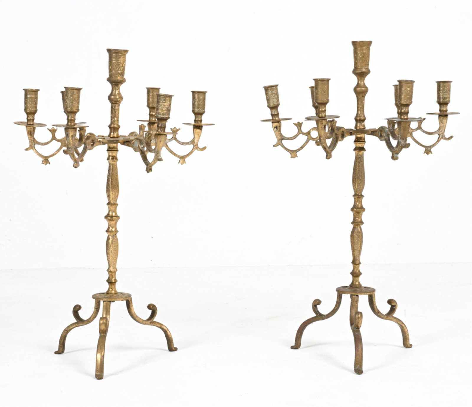 PAIR OF ENGRAVED BRASS CANDELABRAS: Pair of brass candelabras with 6 arms and tripod base. Dimensions: H 22" x Dia. 13.75 ". Conditions: A few bends, small cracks and divots to metal. Mild patination throughout. Surface wear consistent 