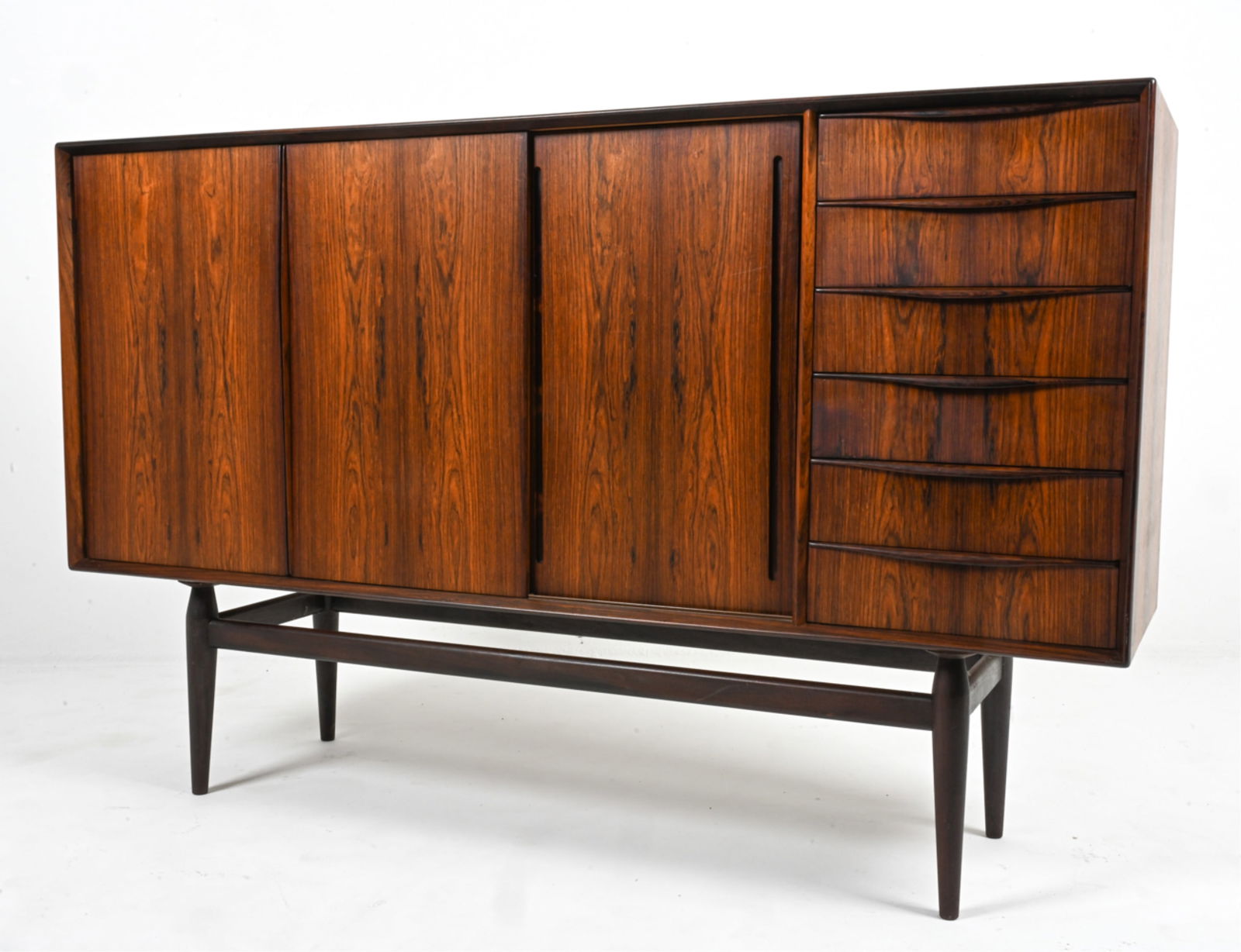 MANNER OF ARNE VODDER ROSEWOOD SIDEBOARD: Mid-Century Modern tall sideboard cabinet in rosewood, featuring sliding doors, dovetailed drawers, and Atomic-inspired tapered legs. In the manner of Arne Vodder for Sibast. Denmark, c. 1960's. Dimen