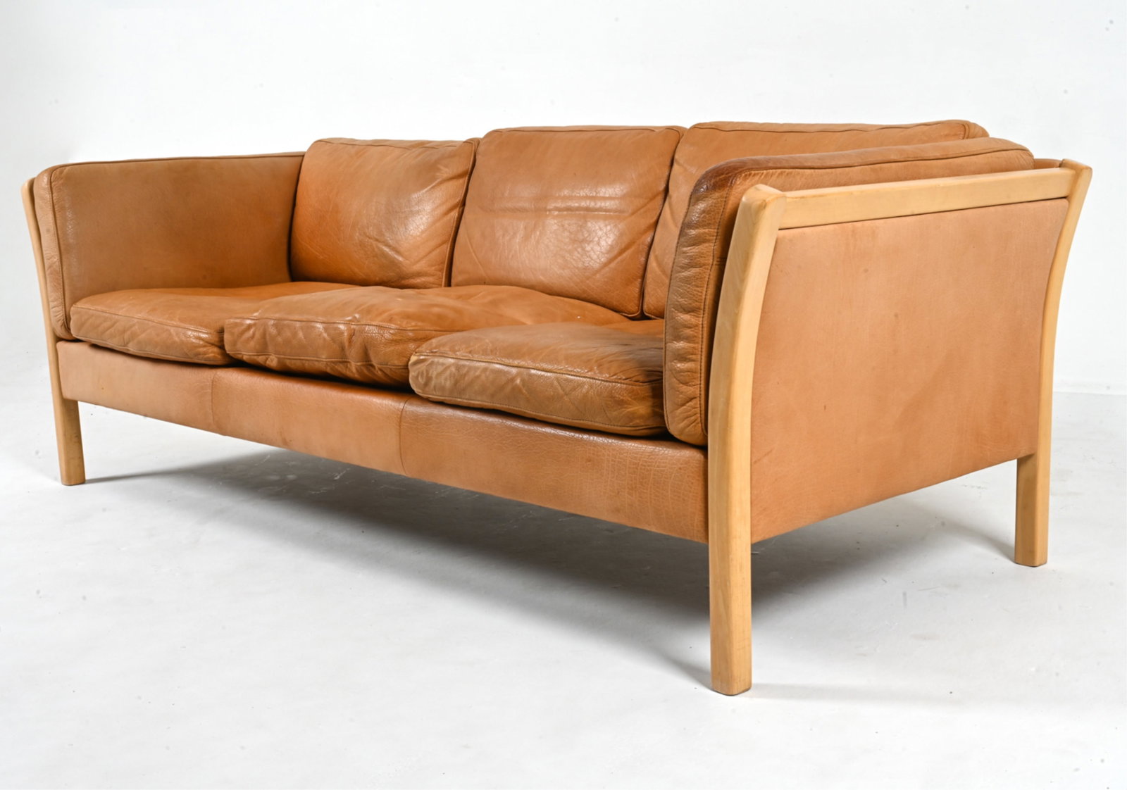 STOUBY THREE-SEAT SOFA IN BEECH & BUFFALO LEATHER: Lined with Stouby logo fabric. Denmark, c. 1970's. Dimensions: H 26.25" x W 79.5" x D 31" x SH 16.25". Condition: Leather with natural patination and surface wear, including sun fading and areas of so