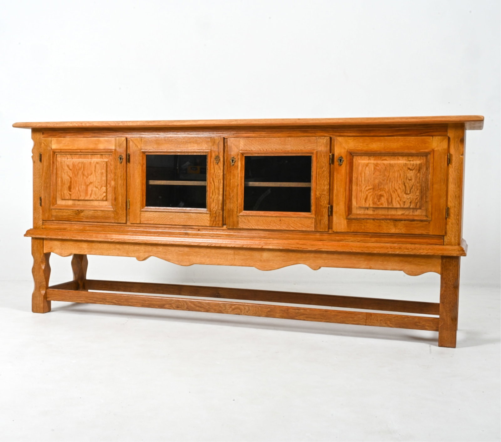 HENNING KJAERNULF DANISH OAK SIDEBOARD, C. 1970'S: Sideboard in quarter-sawn oak, with glazed center doors and raised panel molding at the side doors. Designed by Henning (Henry) Kjaernulf; Denmark, c. 1970's. Key included. Dimensions: H 35.75" x W 82