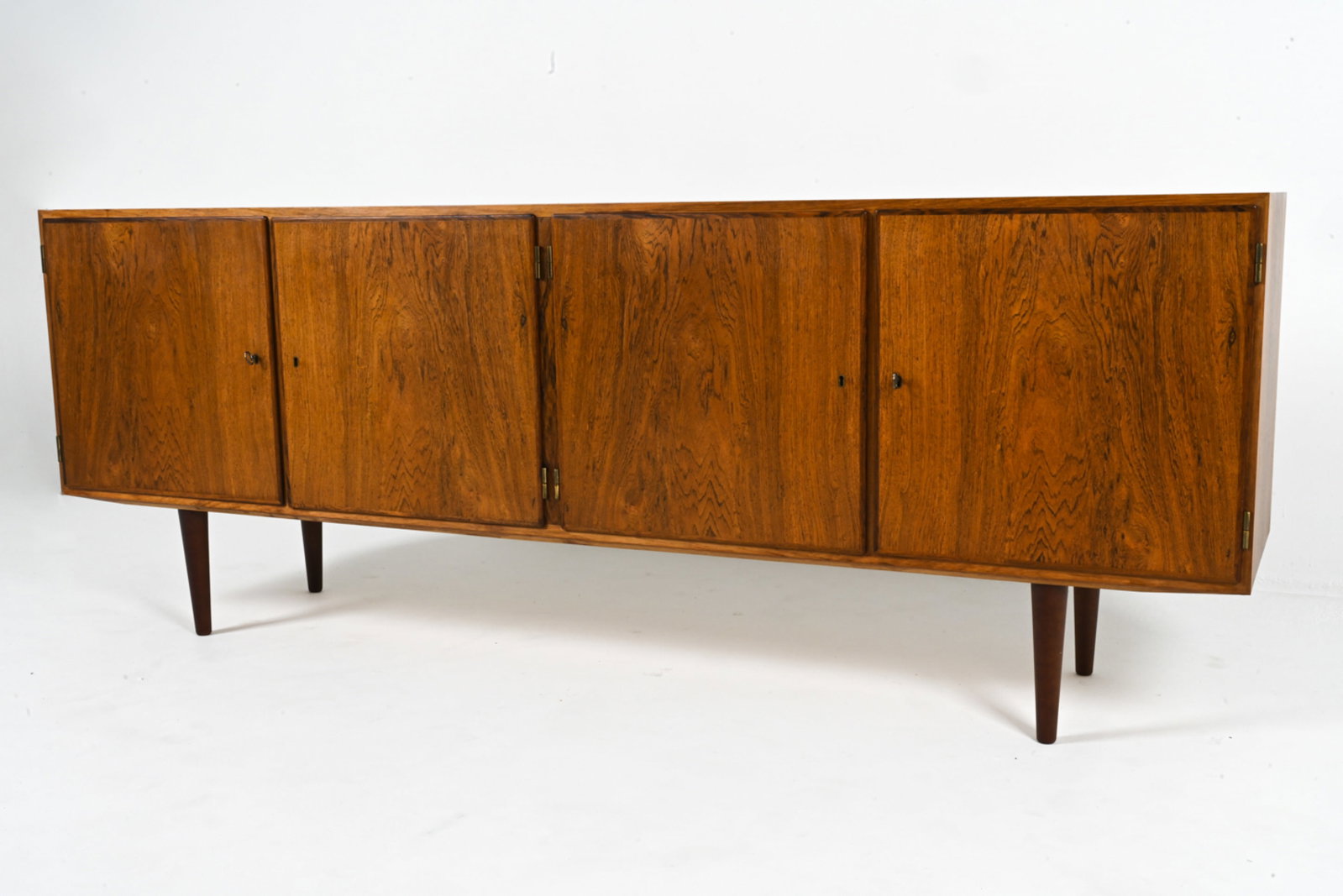 DANISH ROSEWOOD CREDENZA, C. 1960'S: (2) Keys included. Adjustable shelves within each cabinet. Dimensions: H 32" x W 85.25" x D 17". Condition: Legs may not be original. Small scuffs, dents. Small hole cut in back for wires. Uneven fadi