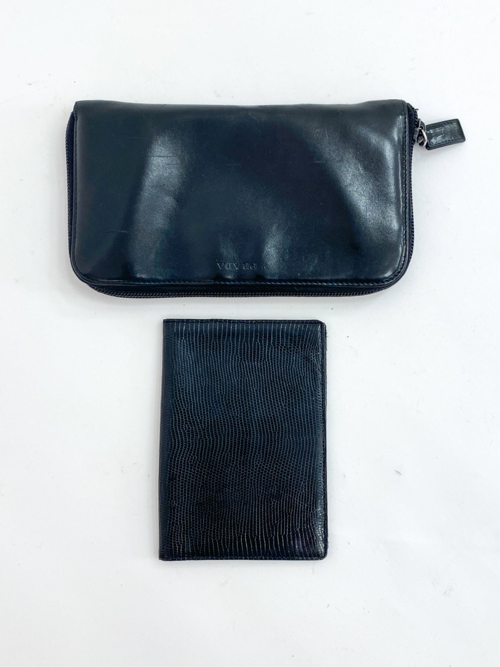 VINTAGE LEATHER WALLETS BY PRADA & MARK CROSS: Genuine Prada black leather zipper pouch, together with a lizard leather bifold wallet by Mark Cross. Dimensions: (Prada) H 4" x W 7.5" x D 1" Condition: Minor scuffs and creases to leather. Prada wal