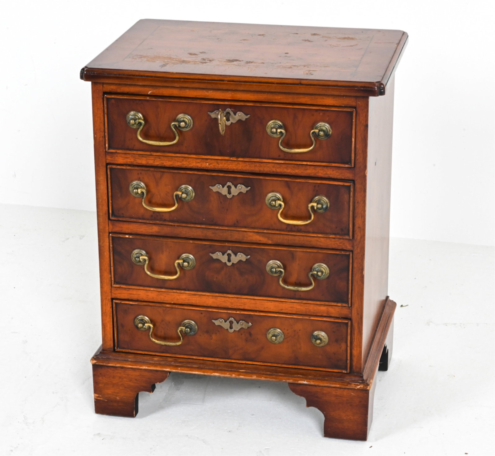MAHOGANY NIGHTSTAND IN THE GEORGIAN STYLE: With antiqued surface, brass pulls. Key included. Circa 1980's. Dimensions: H 22" x W 17" x D 12.75". Condition: Minor losses to finish on top. Missing one pull. Some pulls loose in their brackets.