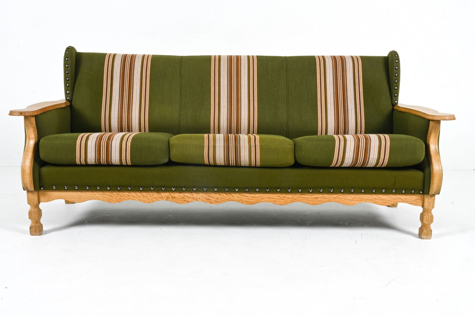 MANNER OF HENNING KJAERNULF OAK SOFA, C. 1970'S: Scandinavian, c. 1970's. Dimensions: H 31" x W 72" x D 28.25" x SH 16.75". Condition: Some wear to fabric from age and use. Light scratches and soiling to wood. Missing one decorative stud at right wi