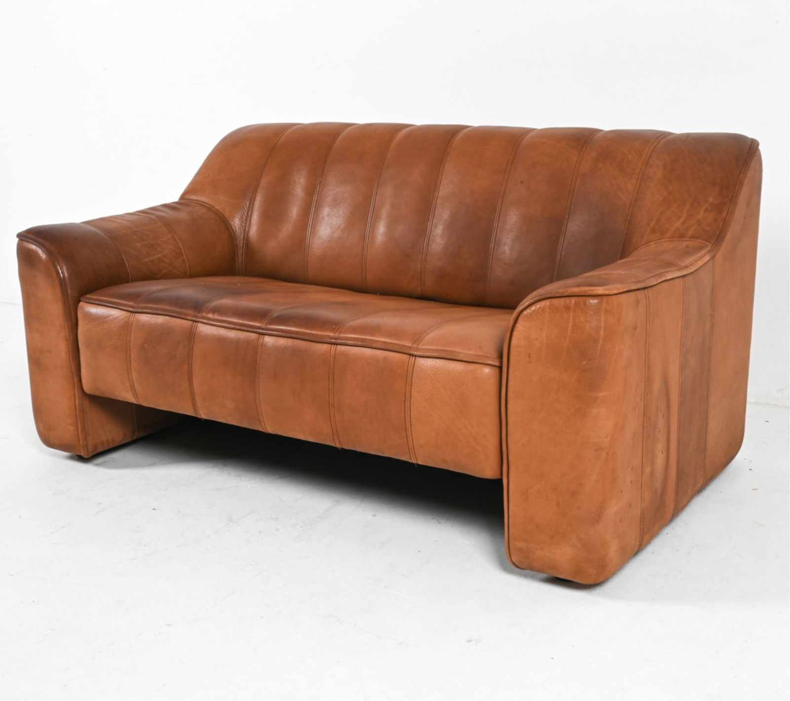 DE SEDE DS-44 BUFFALO LEATHER LOVESEAT: Model DS-44. Seat slightly extends out. Switzerland, circa 1970's. Dimensions: H 27" x W 54" x D 32.25" x SH 15". Condition: Some wear to leather, light scratches and scrapes, some discolored area on