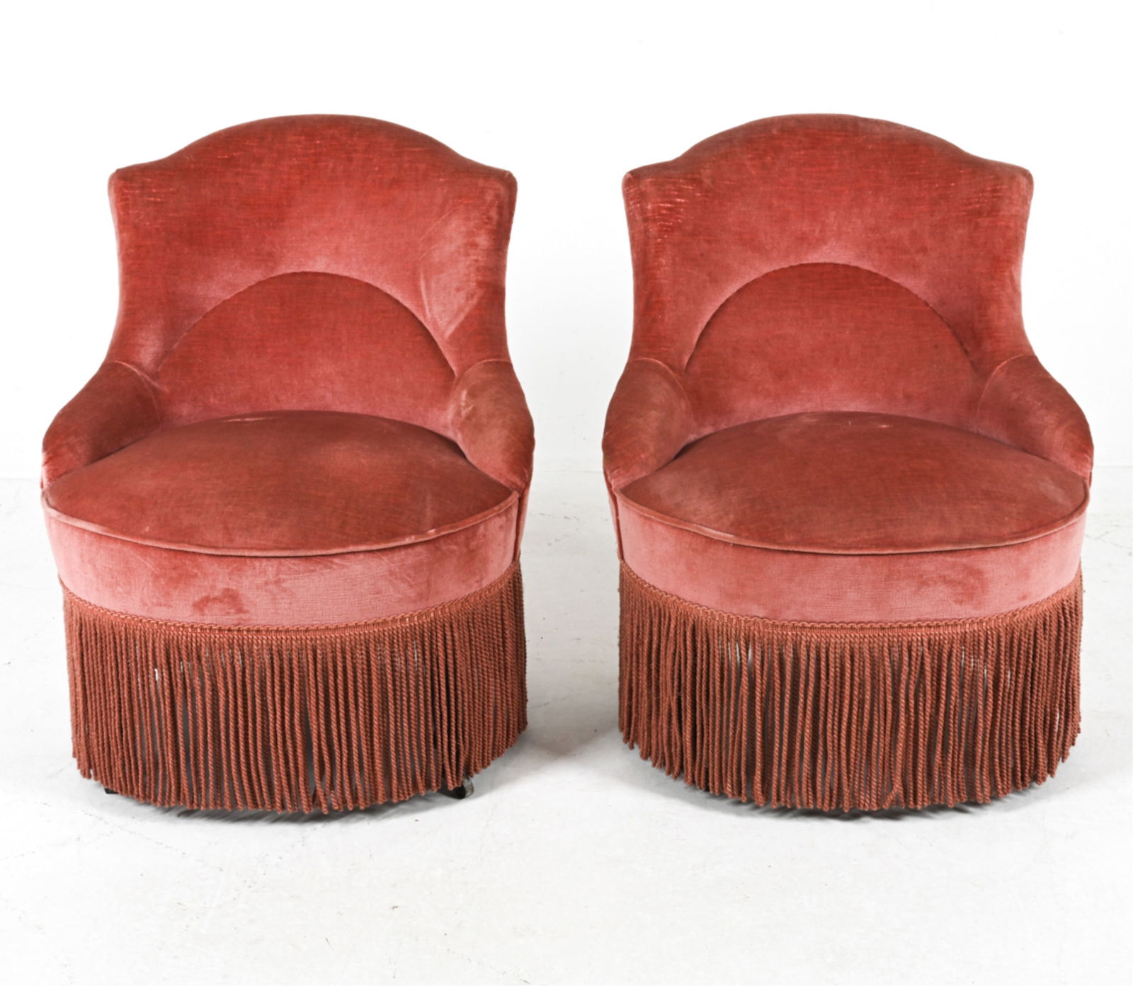 (2) PINK MOHAIR CHAIRS, CIRCA 1950'S: On casters. Upholstered in soft, pink mohair, with a braided fringe. Dimensions: H 31" x W 25" x D 25" x SH 15". Conditions: A few minor areas of balding to fabric. One chair missing casters, some los