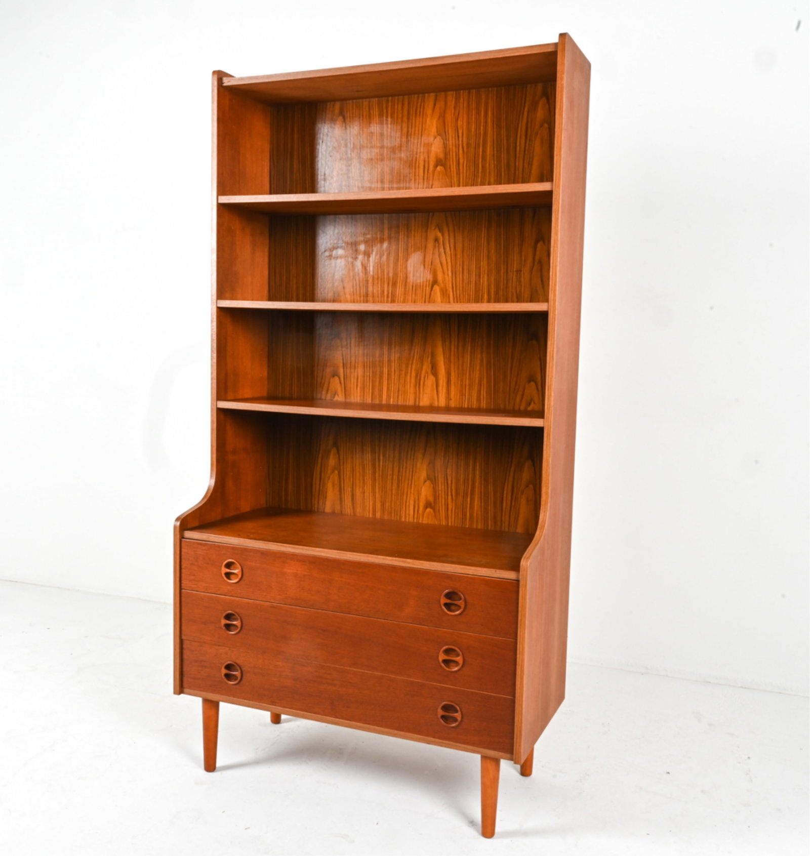 DANISH TEAK STEP-BACK BOOKCASE, C.1960'S: Adjustable shelves, molded round inset drawer pulls. Tapered legs. Dimensions: H 68.75" x W 34.75" x D 16.5" Conditions: Break in top most shelf near dowel on left side. damage to top front corner as 