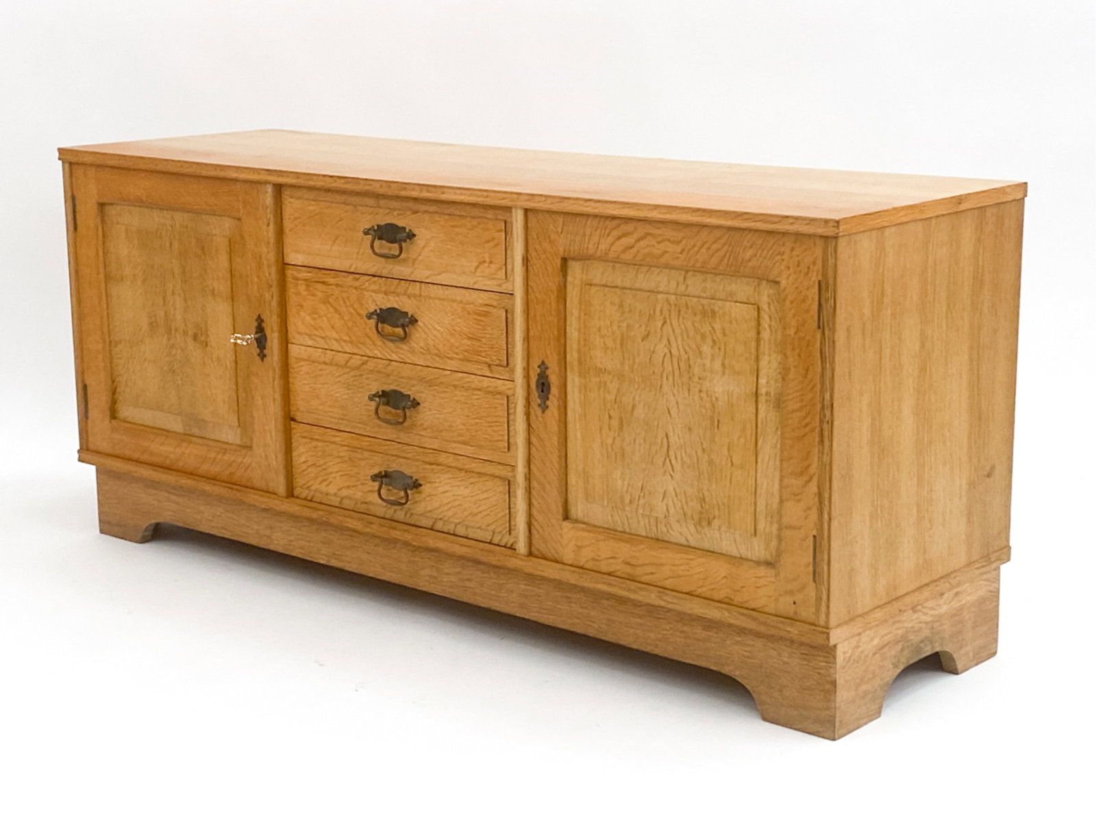 DANISH OAK SIDEBOARD STYLE OF KJAERNULF, C. 1970'S: Oak sideboard in the style of Henning Kjaernulf, with four drawers, brass pulls, and two side compartments with an adjustable shelf in each. Includes key. Unsigned. Dimensions: H 23.75" x W 53.5" x D 