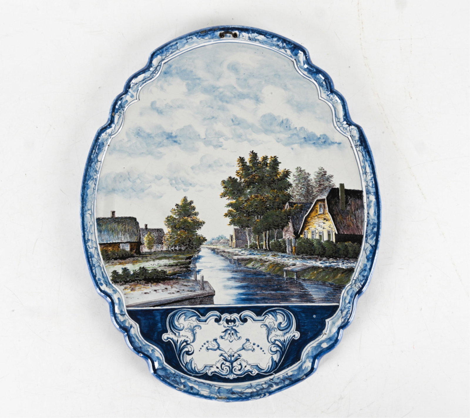 ANTIQUE PORCELAIN DELFT WALL PLAQUE: Signed on back. Polychrome scalloped blue edge depicting shore front houses and figures. Dutch, late 19th or early 20th century. Dimensions: H 22.5" x W 18.25". Condition: Small chips and rubs along r