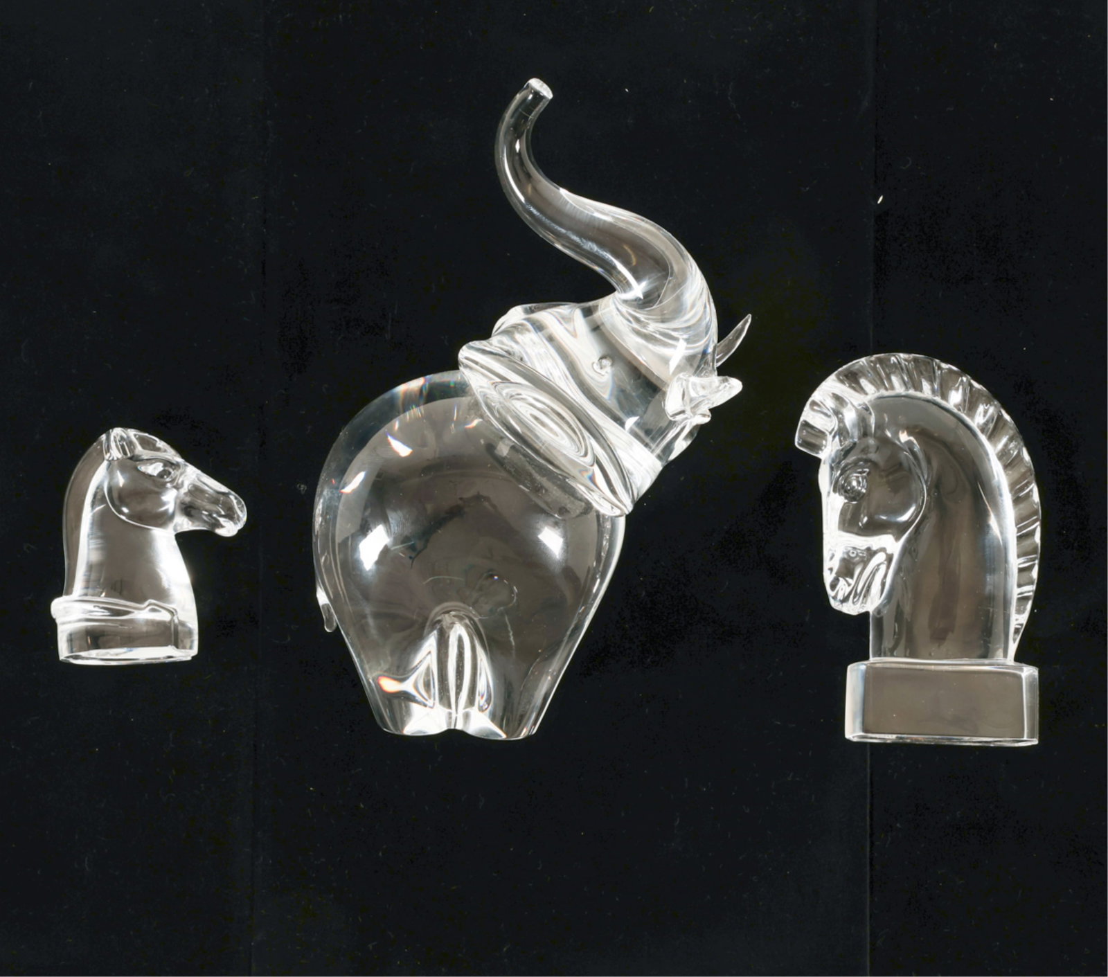 (3) STEUBEN ART GLASS ANIMALS: Includes: Elephant with raised trunk, (2) horses heads. Signed underneath. Dimensions: Elephant H 8" x W 5.25" x D 4.75". Condition: Elephant has one chipped tusk. Very minor surface scratches.