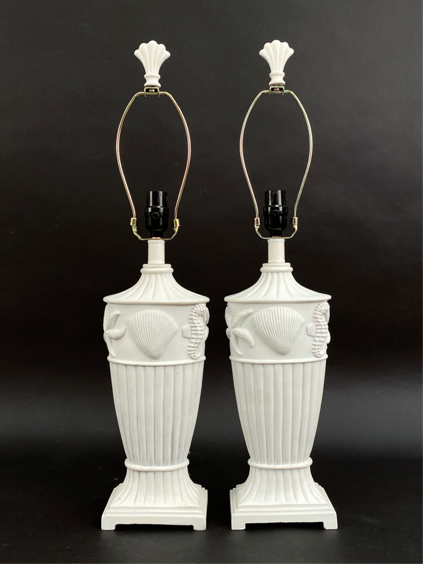 PAIR OF WHITE PAINTED SHELL DESIGN LAMPS: Crafted white sea shell urn lamps. Dimensions: H 29" x W 6" x D 4.25" Condition:. No lamp shades. Not tested. Scattered marks and wear to paint. Warping to harps.