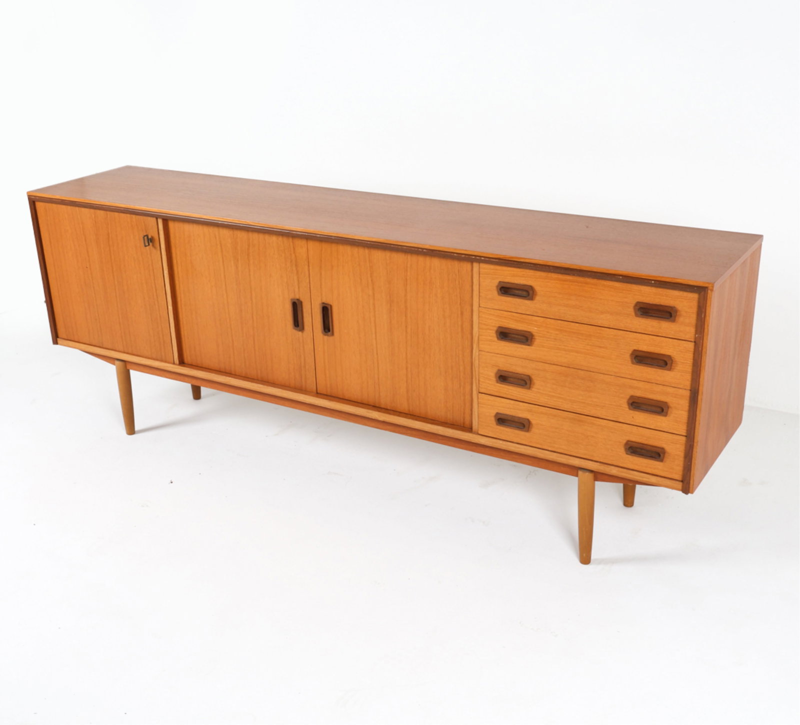 GERMAN TEAK SIDEBOARD, CIRCA 1960'S: (1) Key included. Sculpted inset drawer pulls. Tapered legs. Dimensions: H 32.25" x W 86.25" x D 18.25". Condition: Some scuffs and wear along edges. Faint scratches. Wear consistent with age and use.
