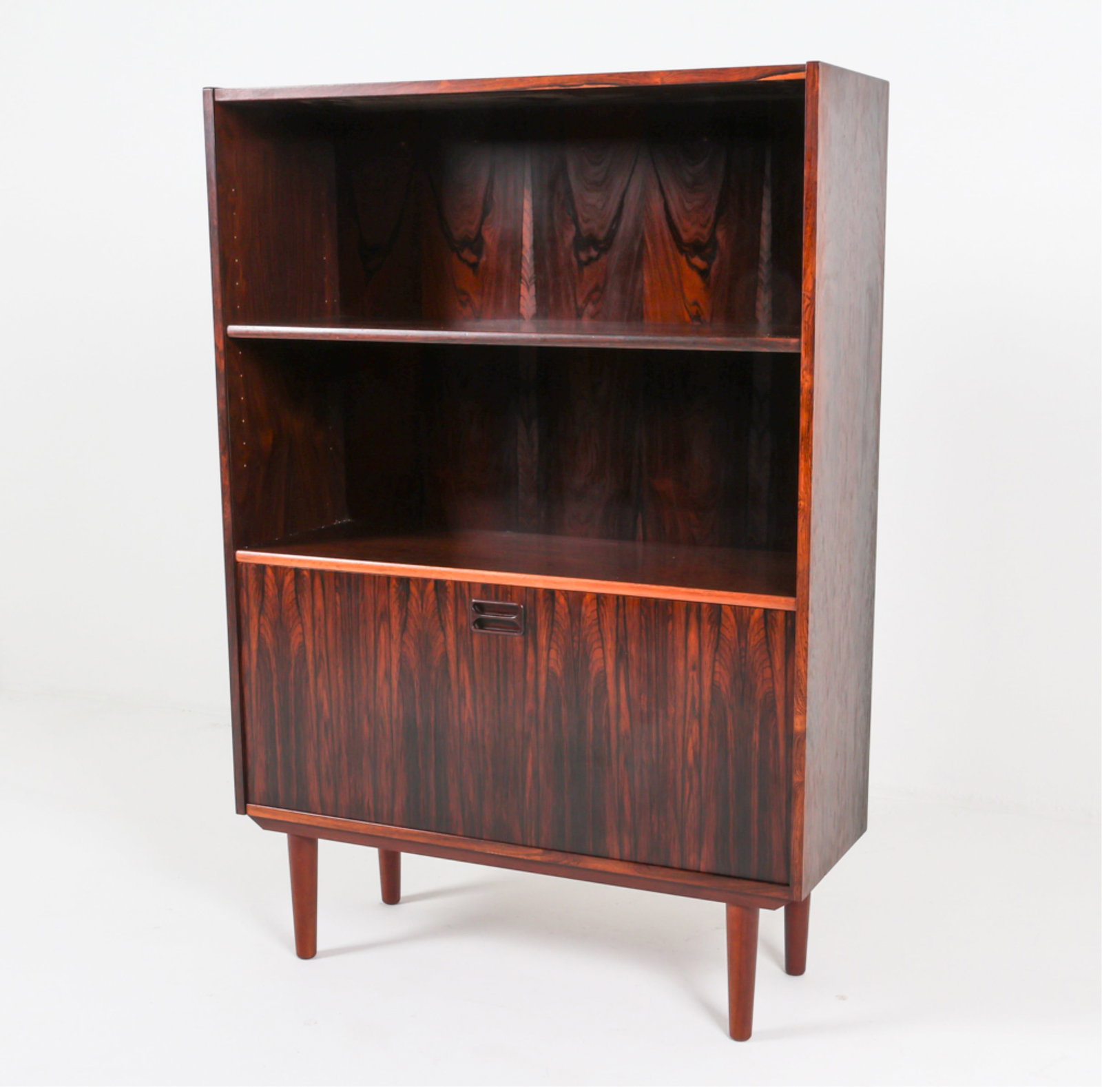DANISH ROSEWOOD BOOKCASE CABINET, C.1960'S: Adjustable shelves. Lower cabinet flips down to reveal dry bar. Tapered legs. Dimensions: H 49.5" x W 34.5" x D 12". Condition: Faint surface scuffs and scratches. Slight musty odor. Wear consistent w