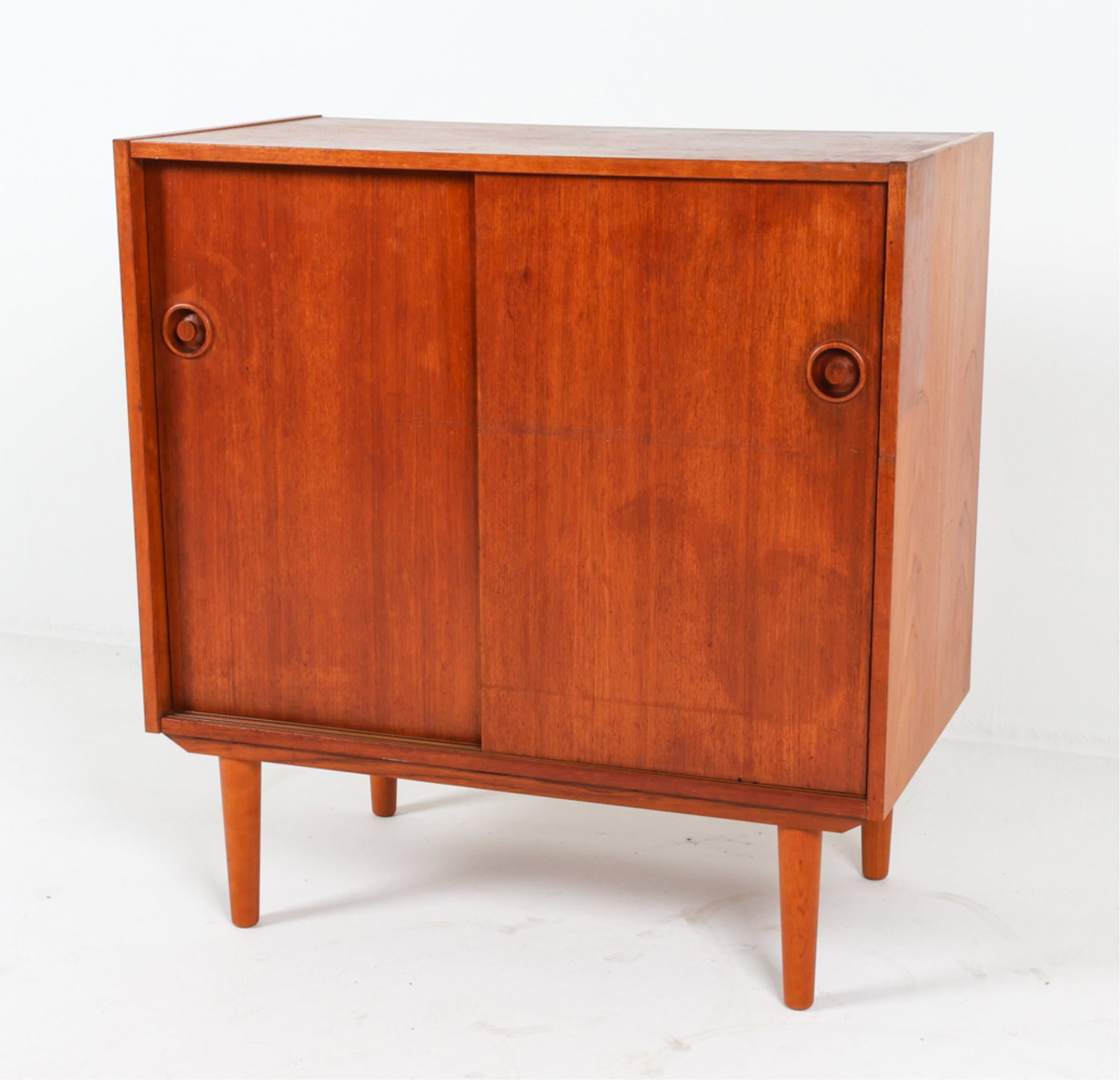 DANISH TEAK CREDENZA CABINET, C.1960'S: Uniquely molded round cabinet door pulls. Tapered legs. Dimensions: H 33" x D 33" x D 17.5". Condition: Some spots of wear to finish, small dings and nicks. Minor chip to veneer on back corner. Wear c