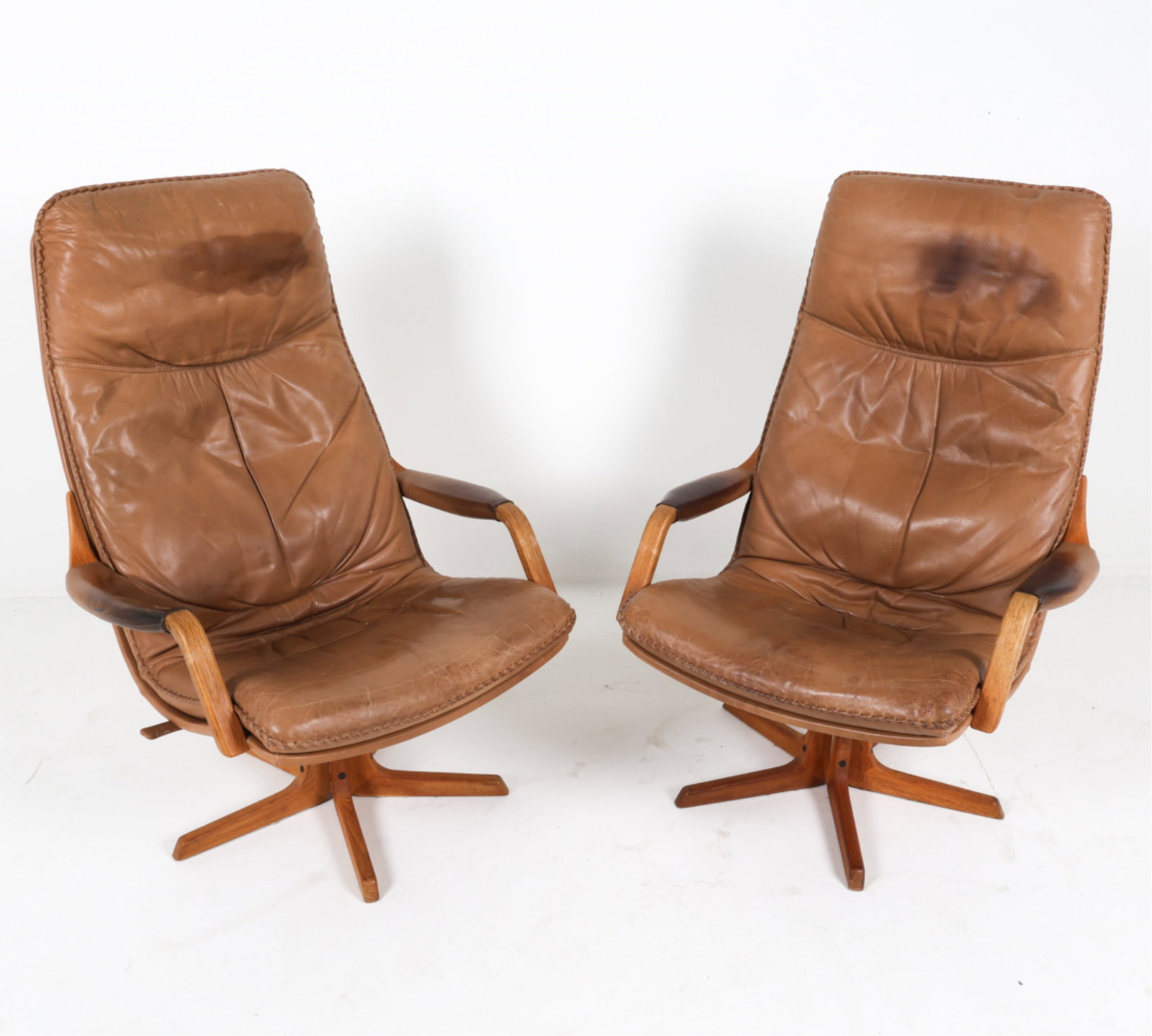 DANISH LEATHER AND OAK LOUNGE CHAIRS FROM BERG: On a swivel base. Woven leather stitched trim on cushions. Circa 1970's. Dimensions: H 43.5" x W 30.25" x D 27.5" x SH 16.5". Condition: Some signs of wear to leather, some creasing and discoloration.