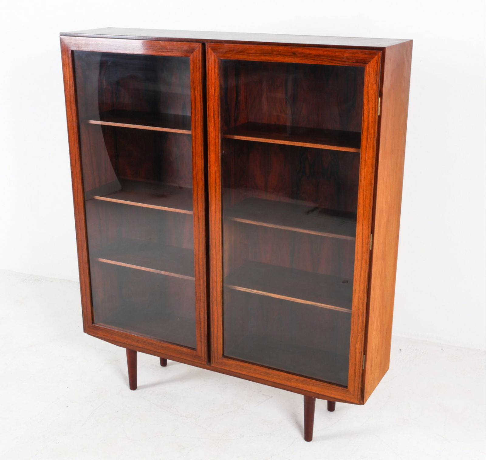 ROSEWOOD BOOKCASE CABINET BY OMANN JUN: Model no. 10. Adjustable shelves. Stands on tapered legs. Dimensions: H 55.75" x W 47.25" x D 12". Condition: Very minor signs of wear, consistent with age and use. DMI095