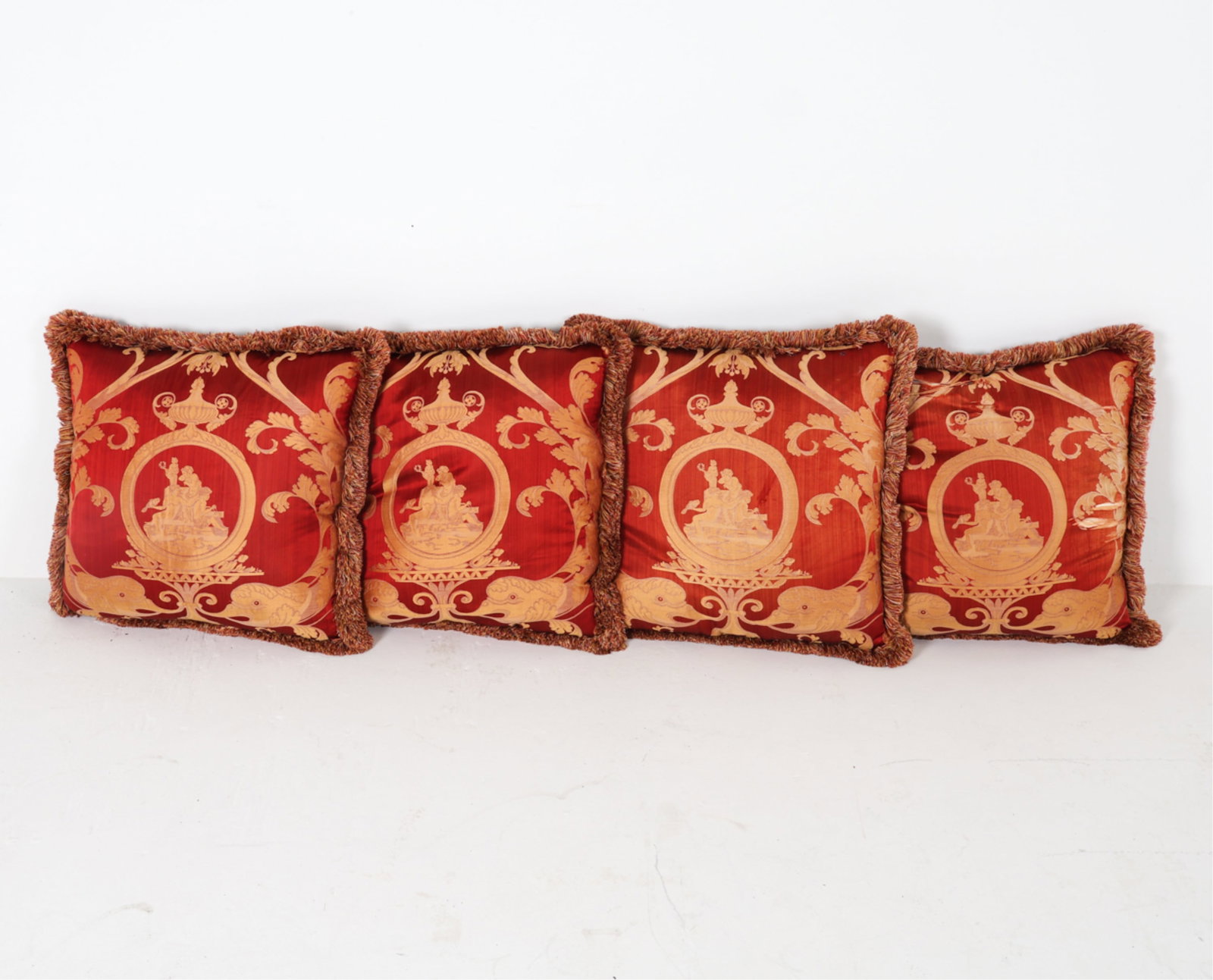 GROUPING OF SILK PILLOWS: Silk pillows, Greco/roman motifs to one side. fringed edges Dimensions: L 25"x W 25" Condition: Wear consistent with age and use, blemishes to edges of fabric. Evident tear to one.