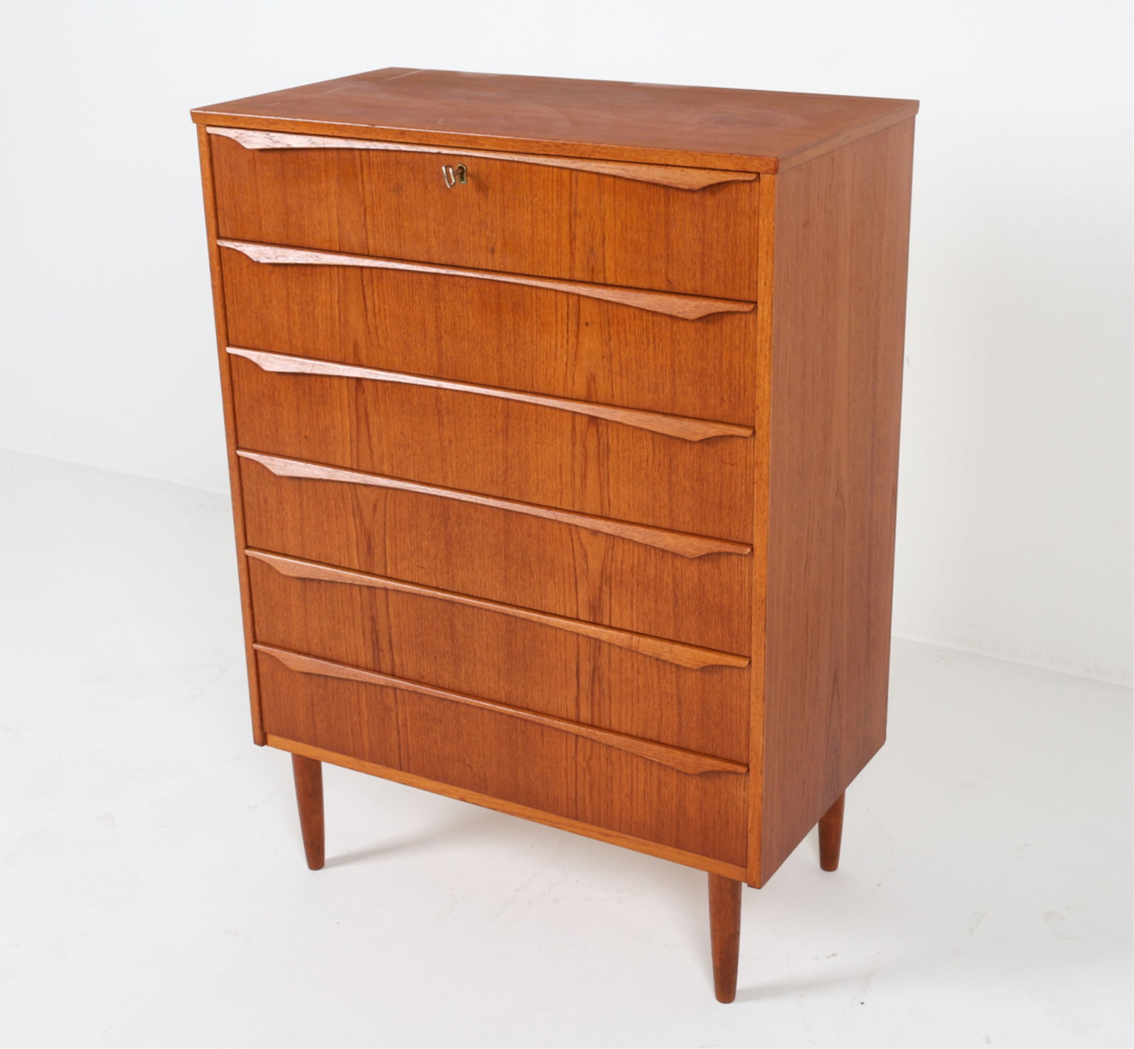 GUNNAR TIBERGAARD NIELSEN TEAK CHEST OF DRAWERS: Key included. Elegantly long sculpted drawer pulls. Tapered legs. Circa 1960's. Dimensions: H 41.5" x W 30" x D 16". Condition: Faint scuffs and dings, wear consistent with age and use. Small chip to