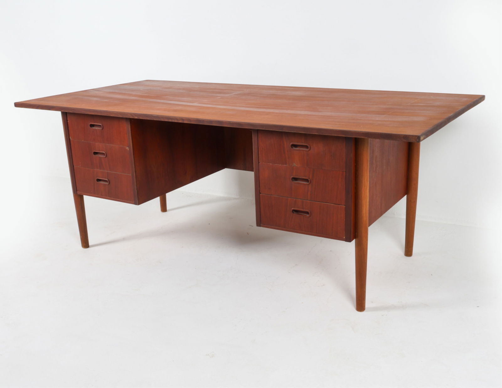 DANISH TEAK WRITING DESK MANNER OF ARNE VODDER: Rounded inset molded drawer pulls. Denmark, circa 1970's. Dimensions: H 28.5" x W 75.25" x D 36.35". Condition: Areas of discoloration and fading on top, faint water rings. Wear consistent with age an