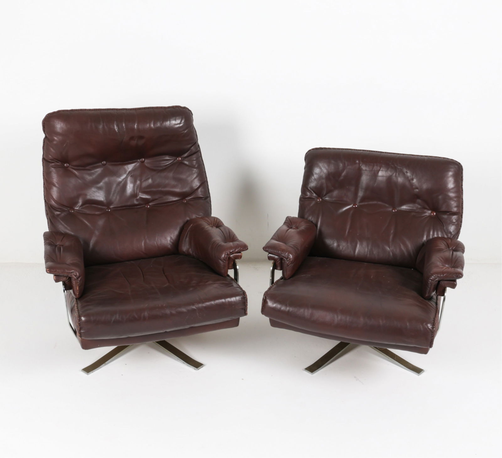 ATTR. ARNE NORELL DANISH SWIVEL ARMCHAIRS C.1970'S: His and hers. Exposed leather stitching. Tufted backs and arms. Chrome swivel base. Dimensions: (Largest chair) H 38" x W 30"x D 39". Seat height 14.75" Condition: Scattered marks and fading to leathe