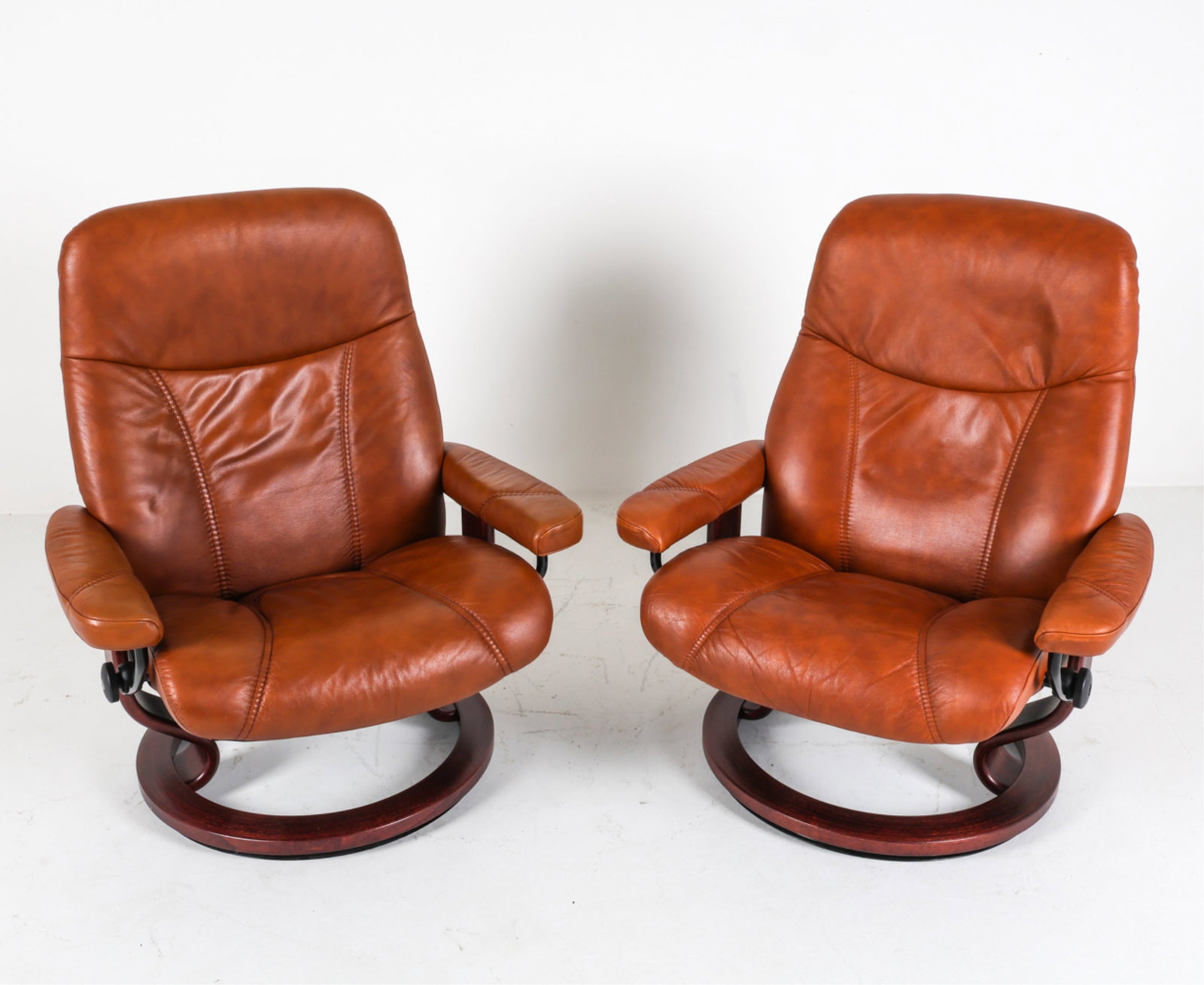 (2) EKORNES 'STRESSLESS' LEATHER & BEECH RECLINERS: Reclining leather lounge chairs on espresso toned beech swivel bases. Large size. Norway, circa 1990's. Dimensions: H 39" x W 33" x D 32" x SH 16.75". W between Arm Rest Bar 26.5". Condition: Minor si