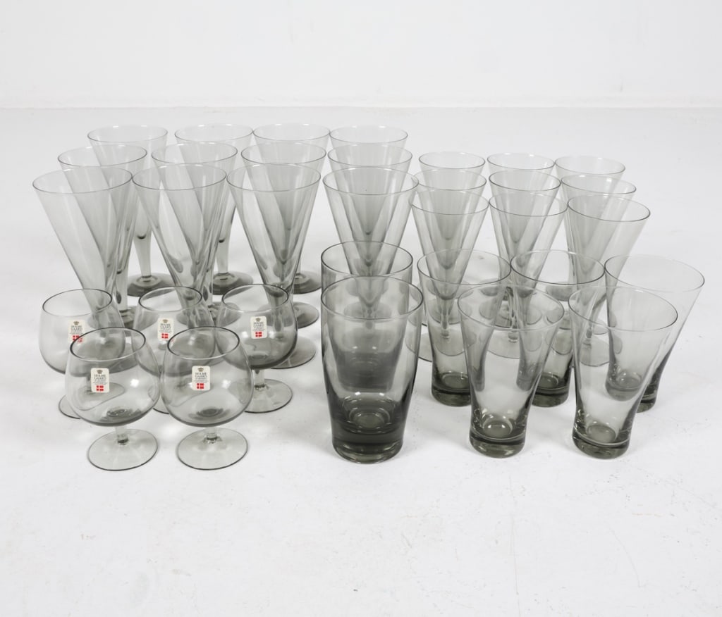 HOLMEGAARD DANISH SMOKE GRAY GLASSWARE: Gradient clear to gray tone bases. Cordial glasses in original boxes. Includes: (12) wine glasses, (9) champagne glasses, (5) glasses, (2) tumblers, (5) cordial glasses. Dimensions: (Largest) H 7.25"