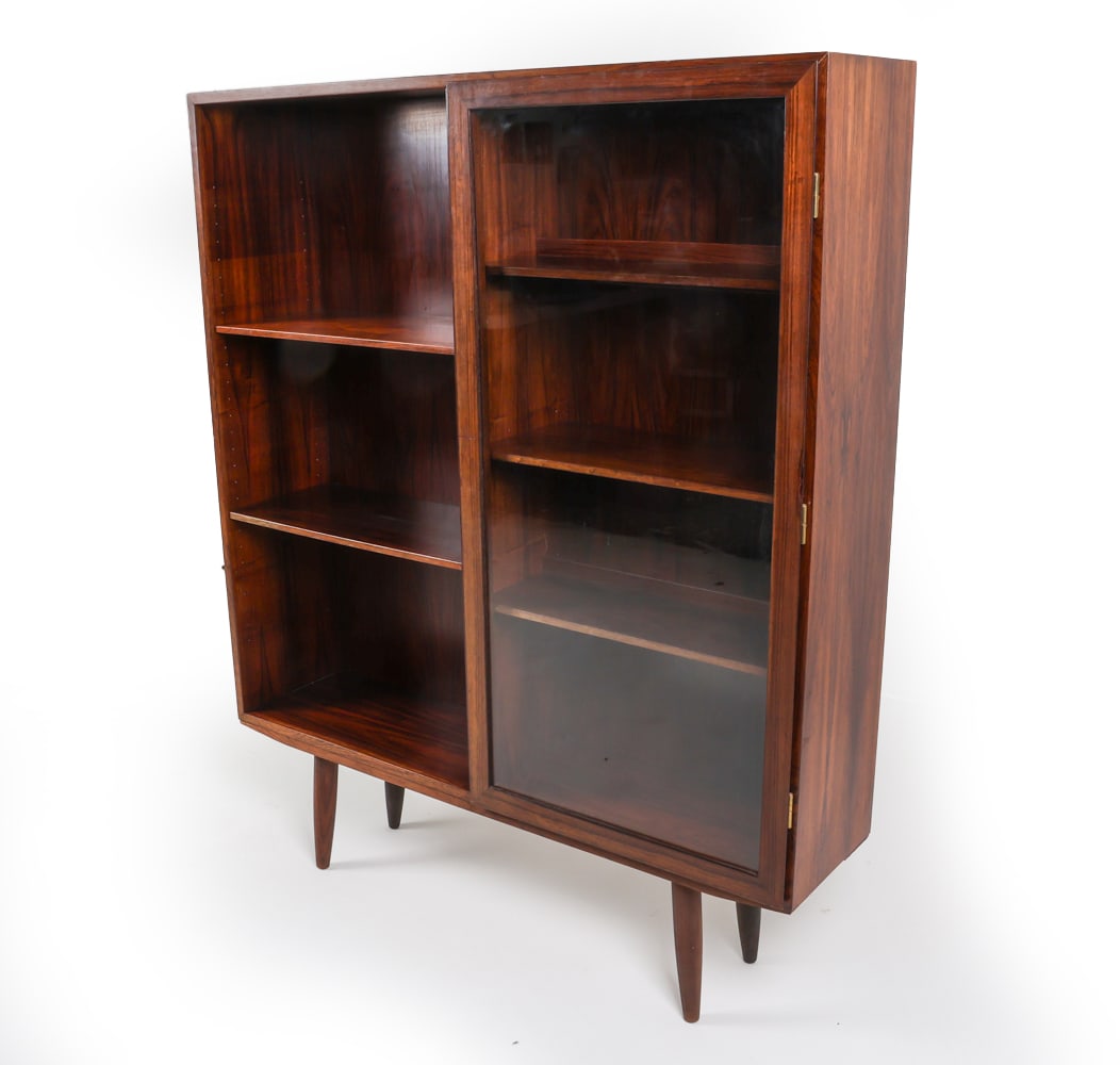 OMANN JUN DANISH ROSEWOOD BOOKCASE C. 1970'S: Adjustable shelves and glass cabinet doors. Lighted shelf. Dimensions: H 58.25" x W 47.5" x D 12" Conditions: Tag on back mostly removed, still visible. Lighting untested. Minor sun fading and a minor