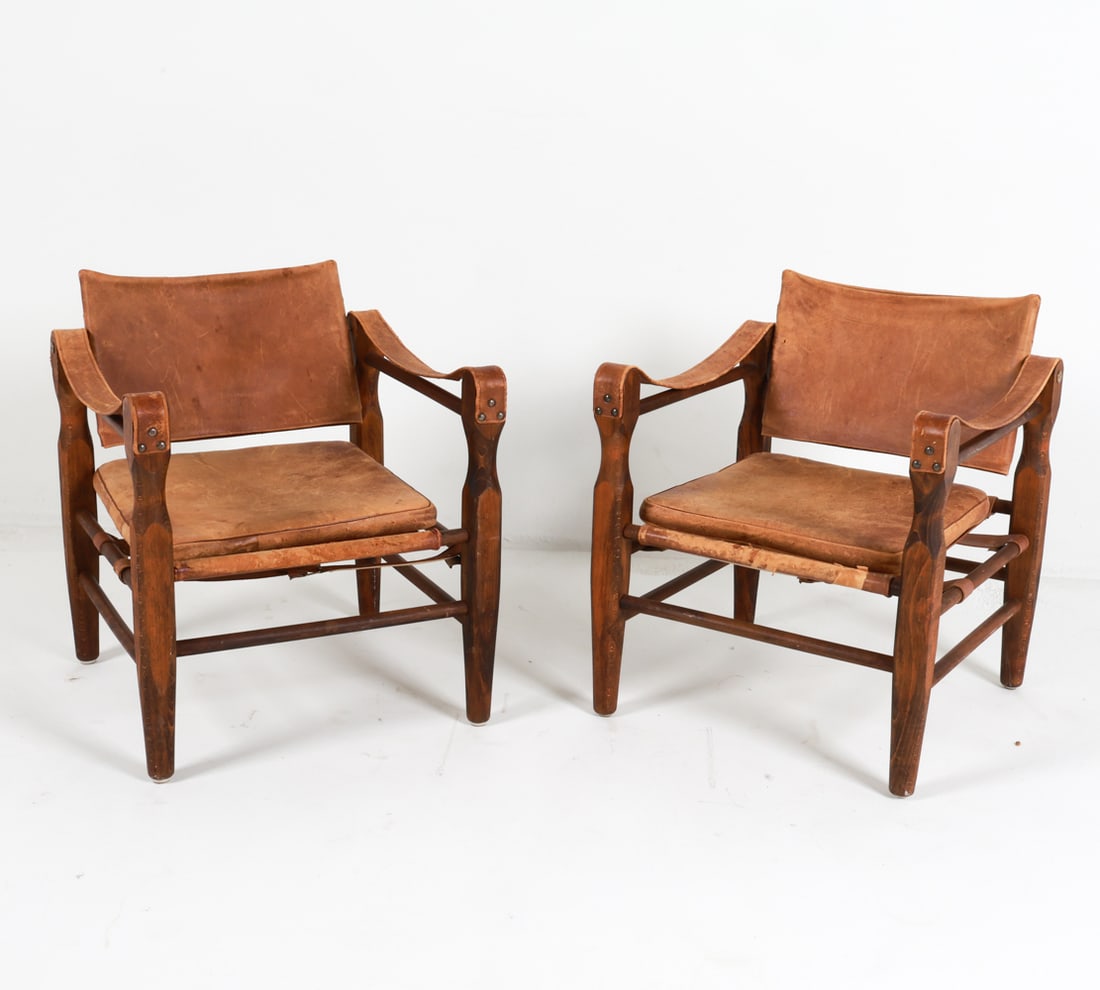 PAIR OF NORELL & KLINT STYLE SAFARI LOUNGE CHAIRS: Beech frames with leather sling upholstery. Brass tacks. Circa 1970's. Dimensions: H 27.75" x W 22.5" x D 22.5" x SH 13.5". Condition: Leather is heavily worn and peeling in places, reupholstering rec