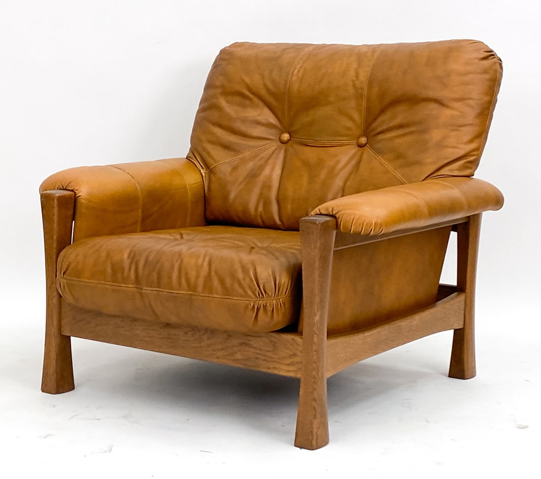 GERMAN BRUTALIST LEATHER LOUNGE CHAIR C. 1970'S: Cognac tone leather upholstery. Oak frame. Dimensions: H 31.5"x W 36"x D 30" Seat height: 15" Condition: Minor indents in leather with sun fading on cushions. Slight separation to stitching on proper 