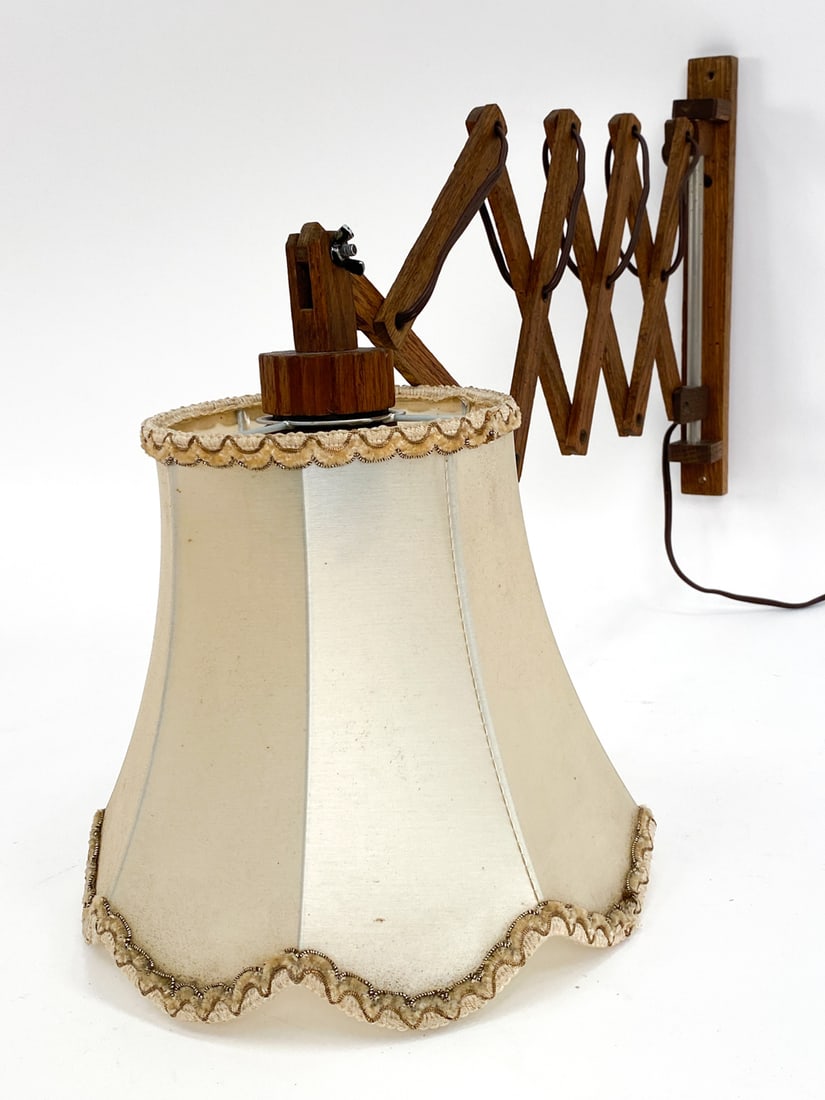 DANISH OAK SCISSOR WALL SCONCE C. 1960'S: Extending arm. With woven fabric shade with embroidered edges. Dimensions: H 11.5" x W 1,25" x D 12" Condition: Minor rubbing. With European plug. Untested. Tarnishing to metal frame of shade. Wear co
