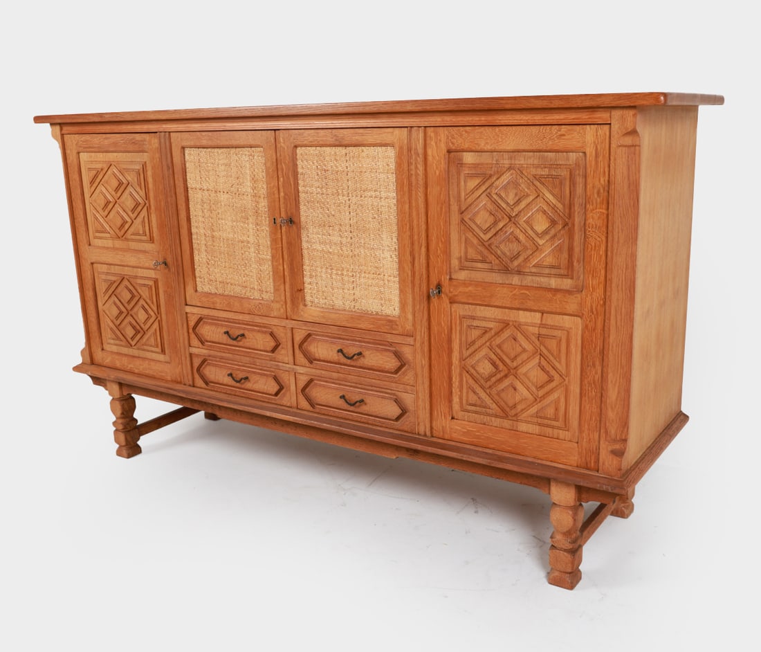 KJAERNULF STYLE DANISH OAK SIDEBOARD C. 1970'S: Includes key. Carved relief doors and woven rattan panel center doors. Dimensions: H 46.25" x W 81" x D 21". Condition: Slight scuffs and marks on wood. Wear consistent with age and use. Presents well