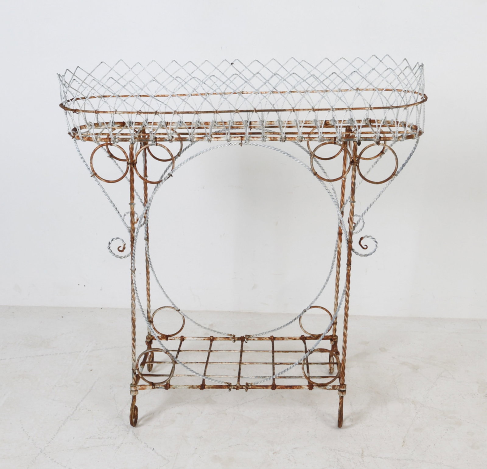 WROUGHT IRON PLANT STAND: Cross hatched design with spiral feet and accents. 20th century. Dimensions: H 34.5" x W 33.5" x D 13.5" Condition: Evident oxidation to planter. Wear consistent with age and outdoor use.