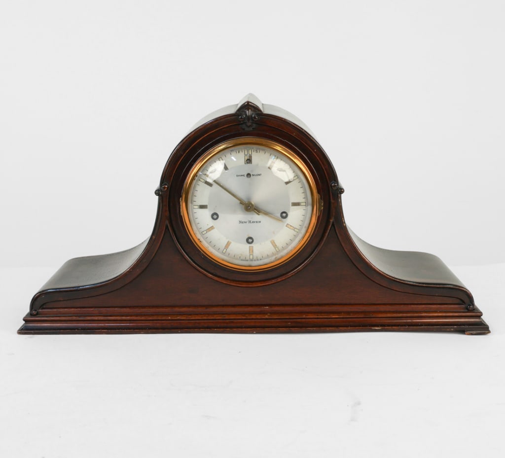 NEW HAVEN MANTEL CLOCK: Marked to interior. Eight day pendulum chime clock. Dimensions: H 10.25" x W 20.25" x D 6" Condition: Nicks and rubbing on edges. Clock face convex glass needs repair. Scuffs and scratches on veneer.