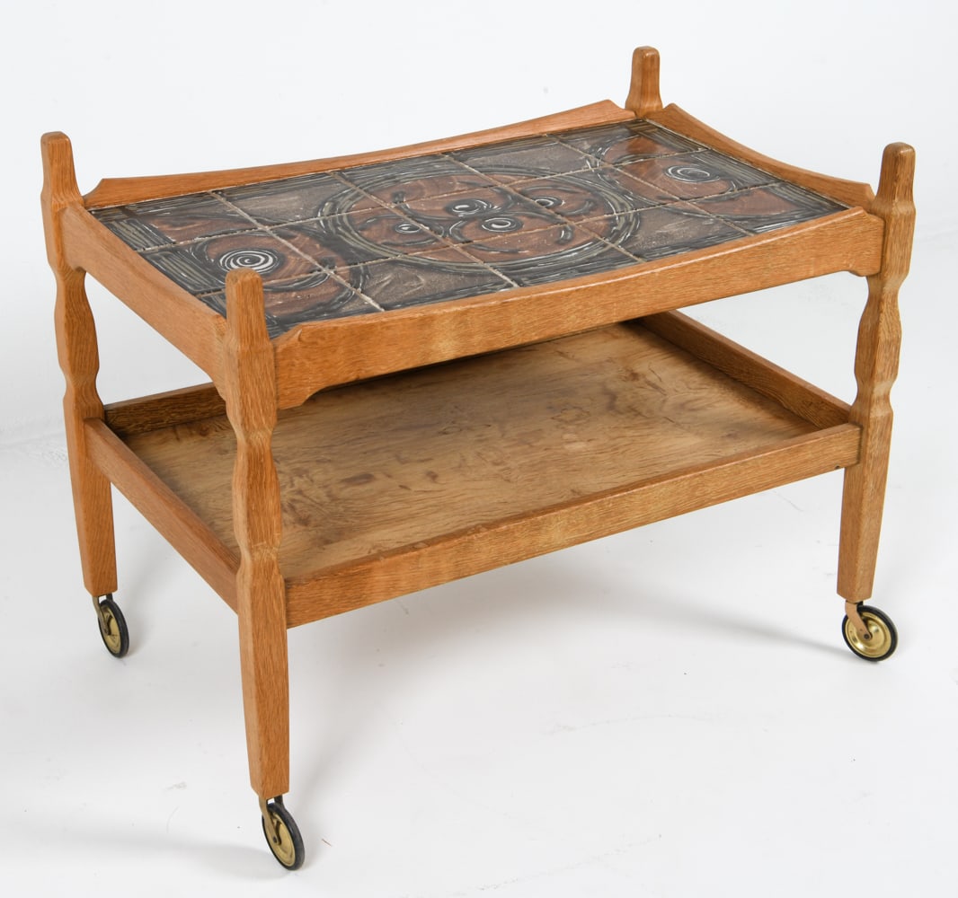 KJAERNULF STYLE OAK & TILE SERVING CART C. 1970'S: Danish. Oak serving cart on brass casters, with tile top. Dimensions: H 26" x W 32.75" x D 21" Condition: Wheels may require lubrication. Rubbing and discoloration to oak edges. Wear consistent with a