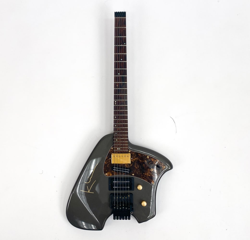 KLEIN HEADLESS ELECTRIC GUITAR GRAY FINISH 1990S: c. 1990s. Gray finish on body. Rosewood fingerboard with abalone dot inlay on top, and mother of pearl dot inlay on the side. Gold and black hardware. Solid rosewood neck. Condition: Chips on the fron