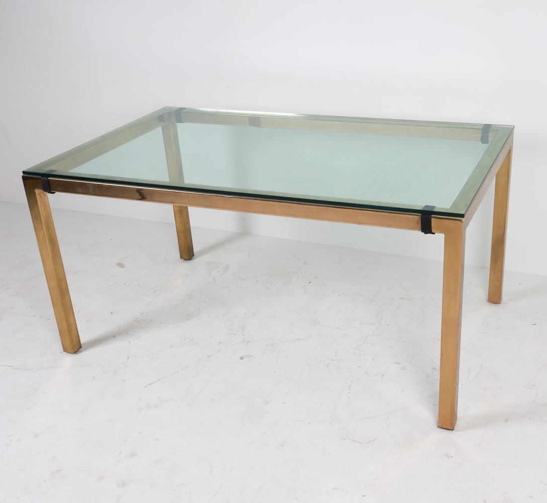 BRASS AND GLASS DINING TABLE: Brass frame with smoked glass top. Dimensions: H 50" x W 60.25" x D 36" Condition: Scattered marks and creases on frames. Wear consistent with age and use.