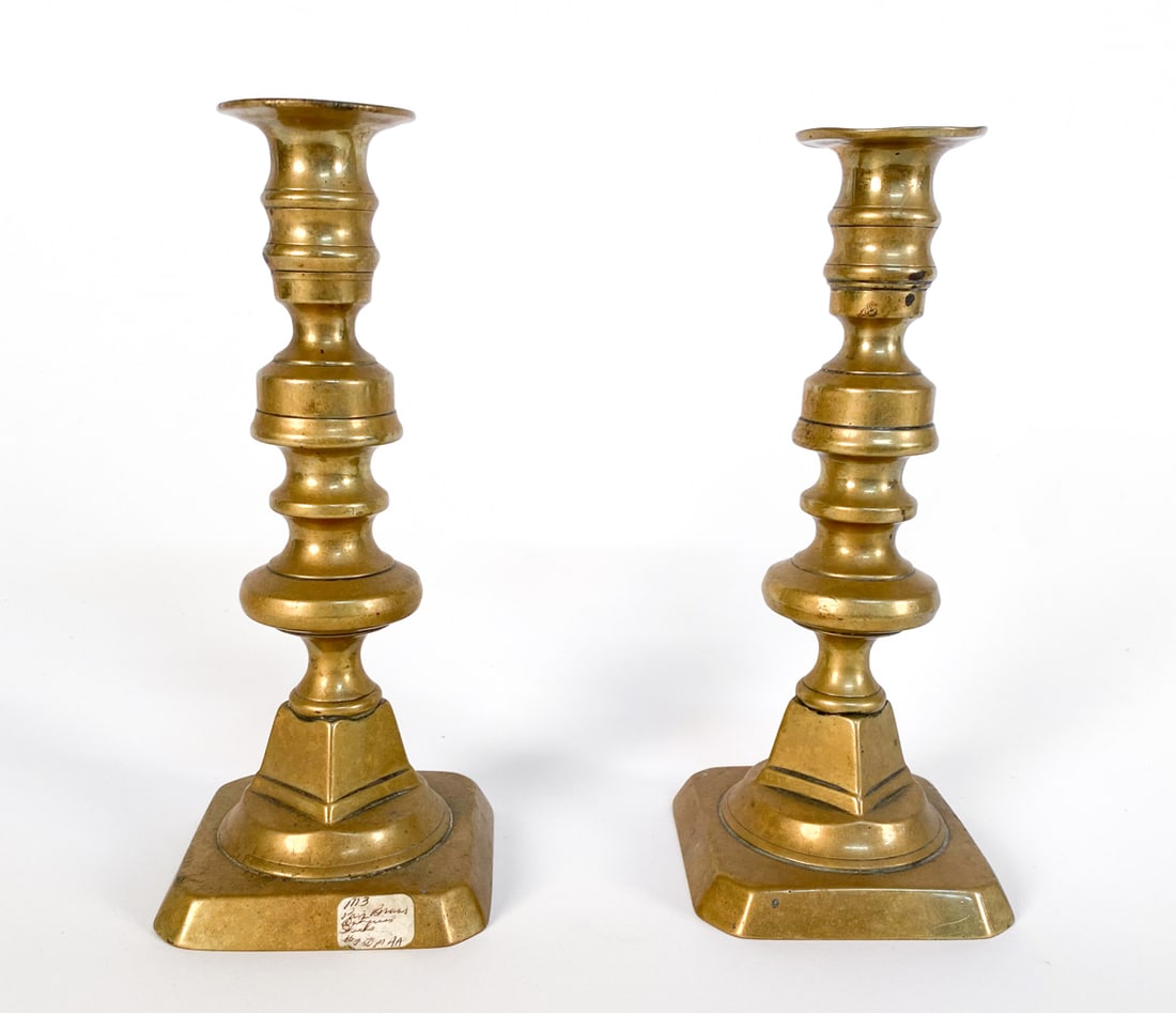 PAIR ANTIQUE ENGLISH BRASS CANDLE STICKS: Dimensions: H 8"x W 3.25" x D 3.25" Condition: Scattered spots of tarnishing on brass. Candle and wax residue to interior. Slight warp to top rims. Wear consistent with age and use.